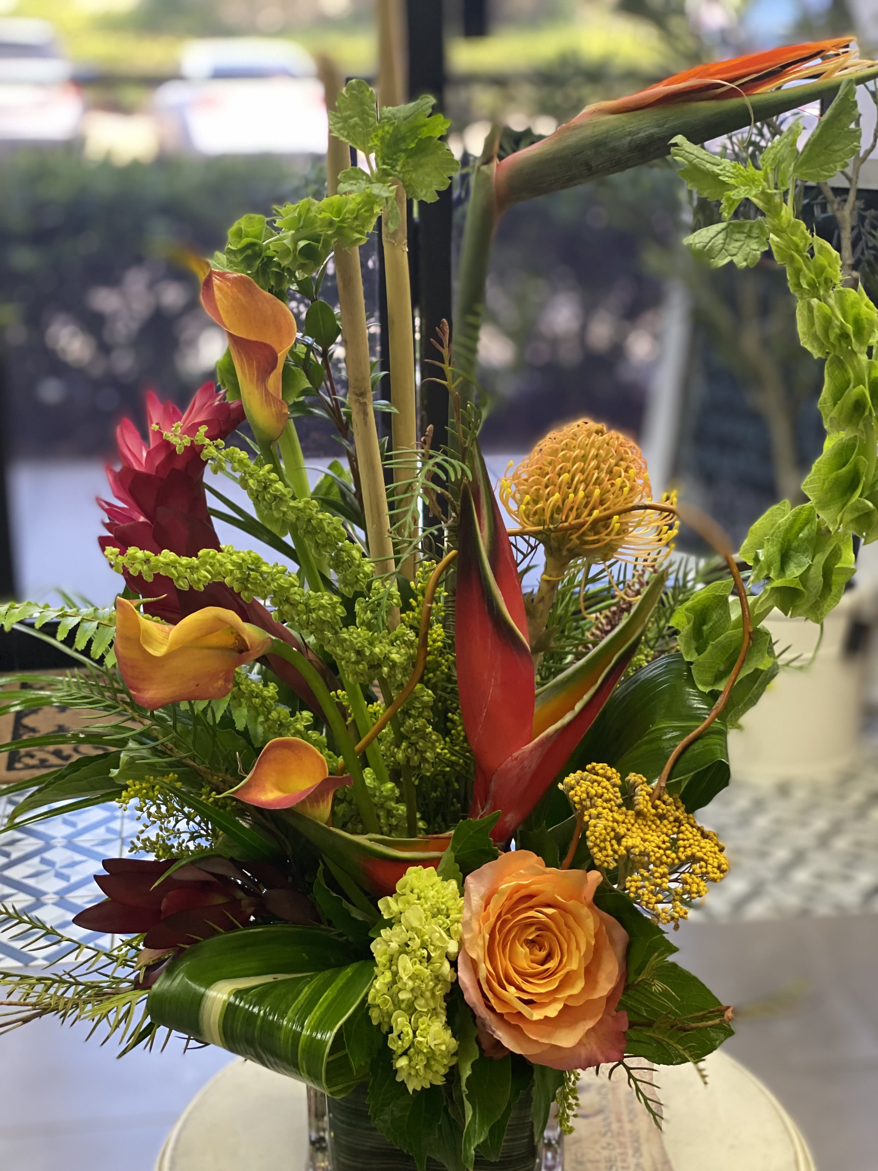 Tropical floral arrangement with orange roses and calla lilies in a glass vase