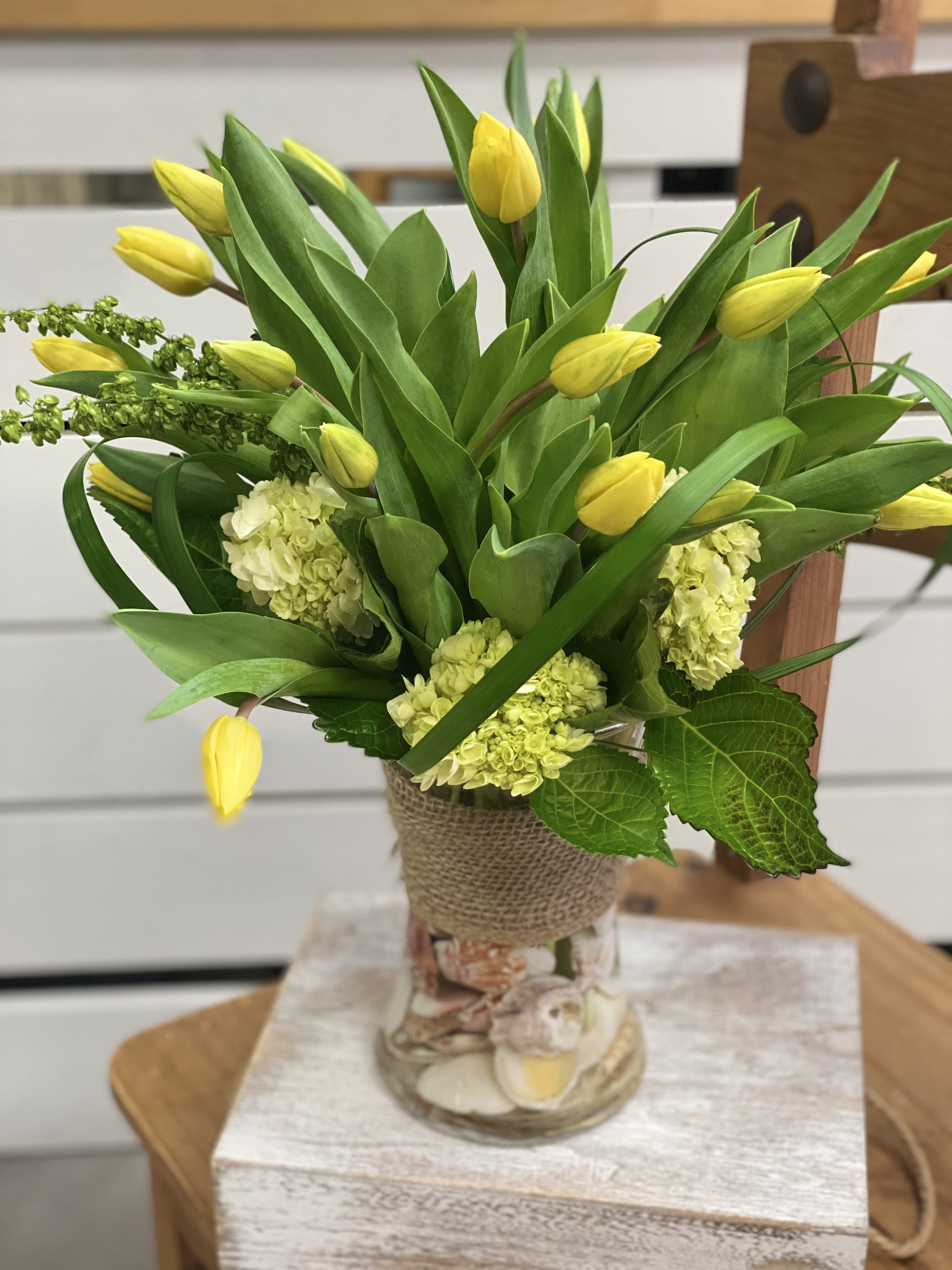 Yellow tulips and pale green hydrangeas in a glass vase wrapped with burlap