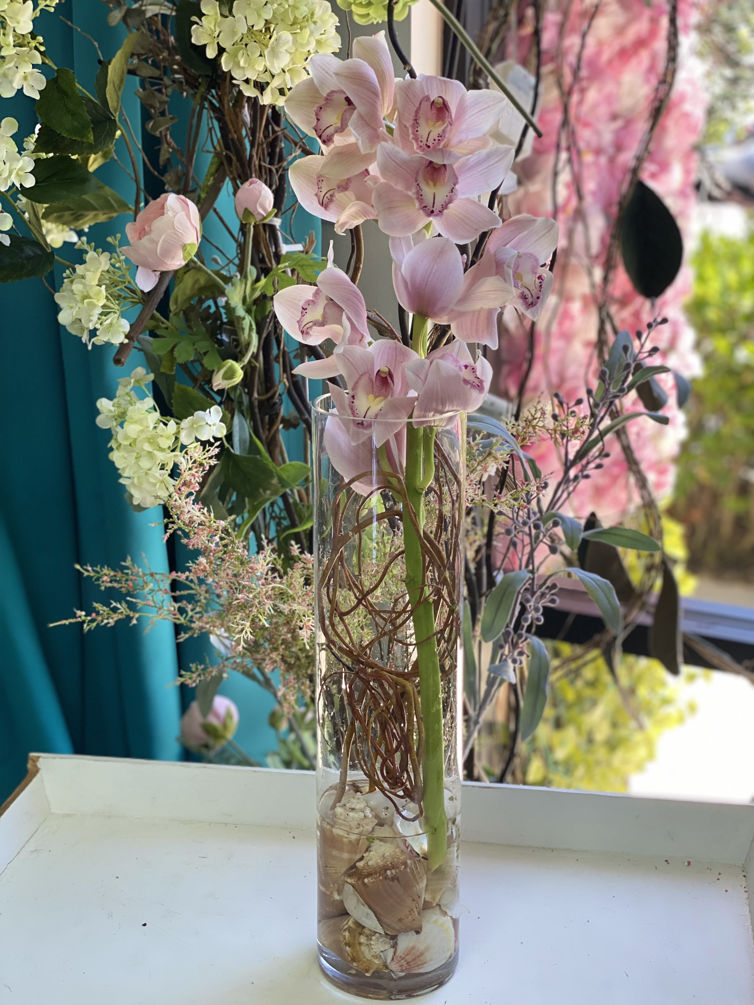 Pink orchids arranged in a tall glass vase with decorative branches