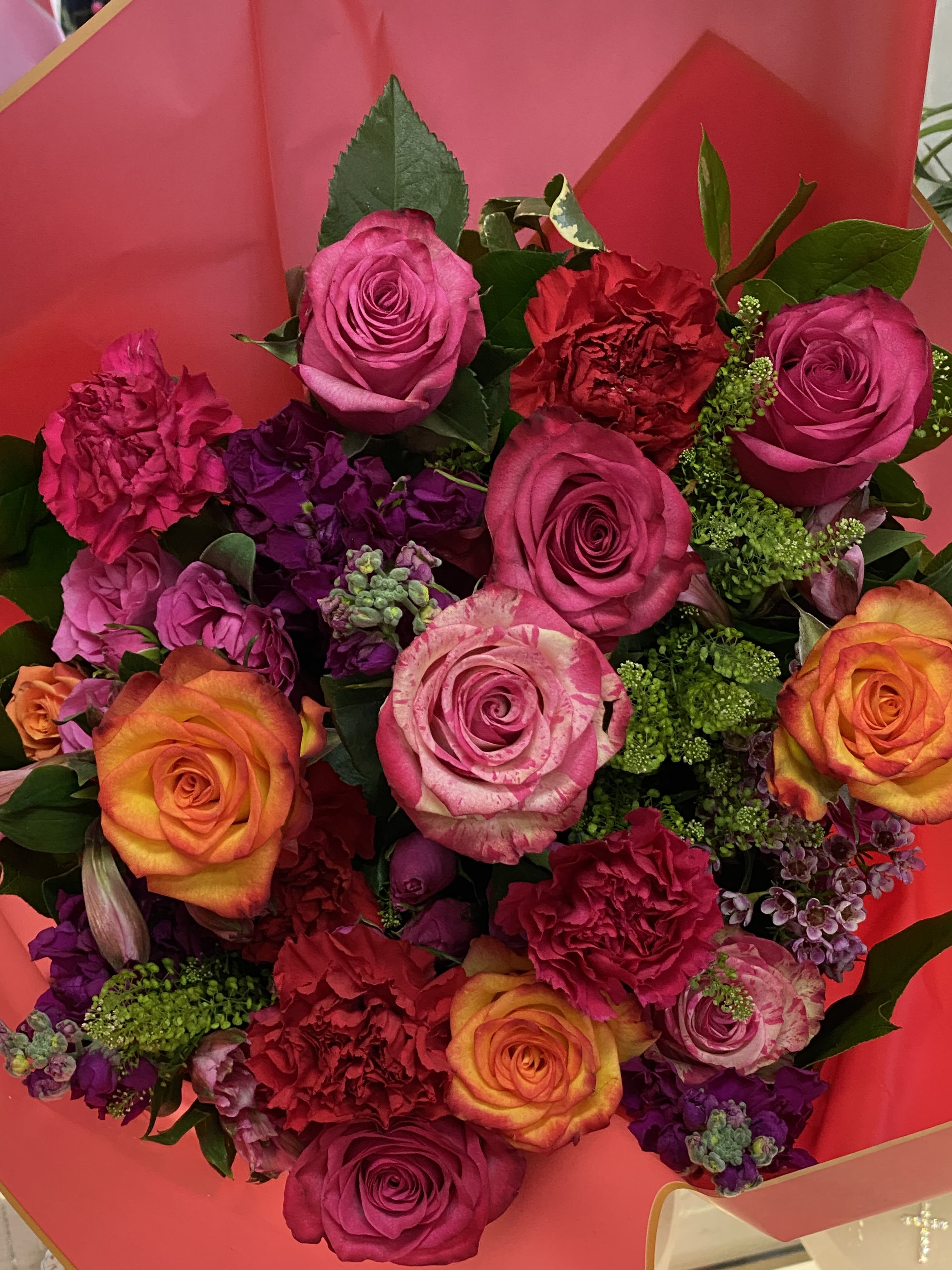 Bouquet of pink, orange, and purple roses with carnations in red wrapping