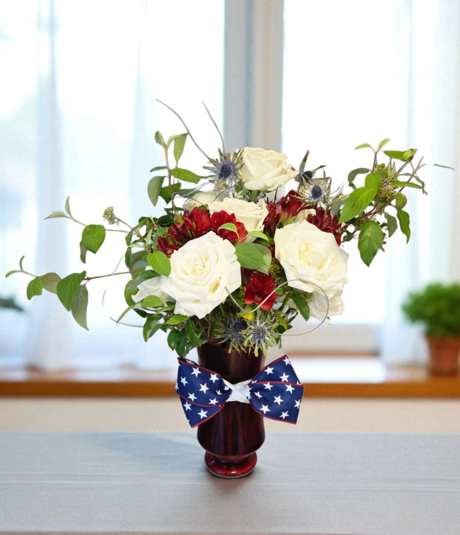 Patriotic red, white, and blue flower arrangement in a red vase with a star-spangled bow.