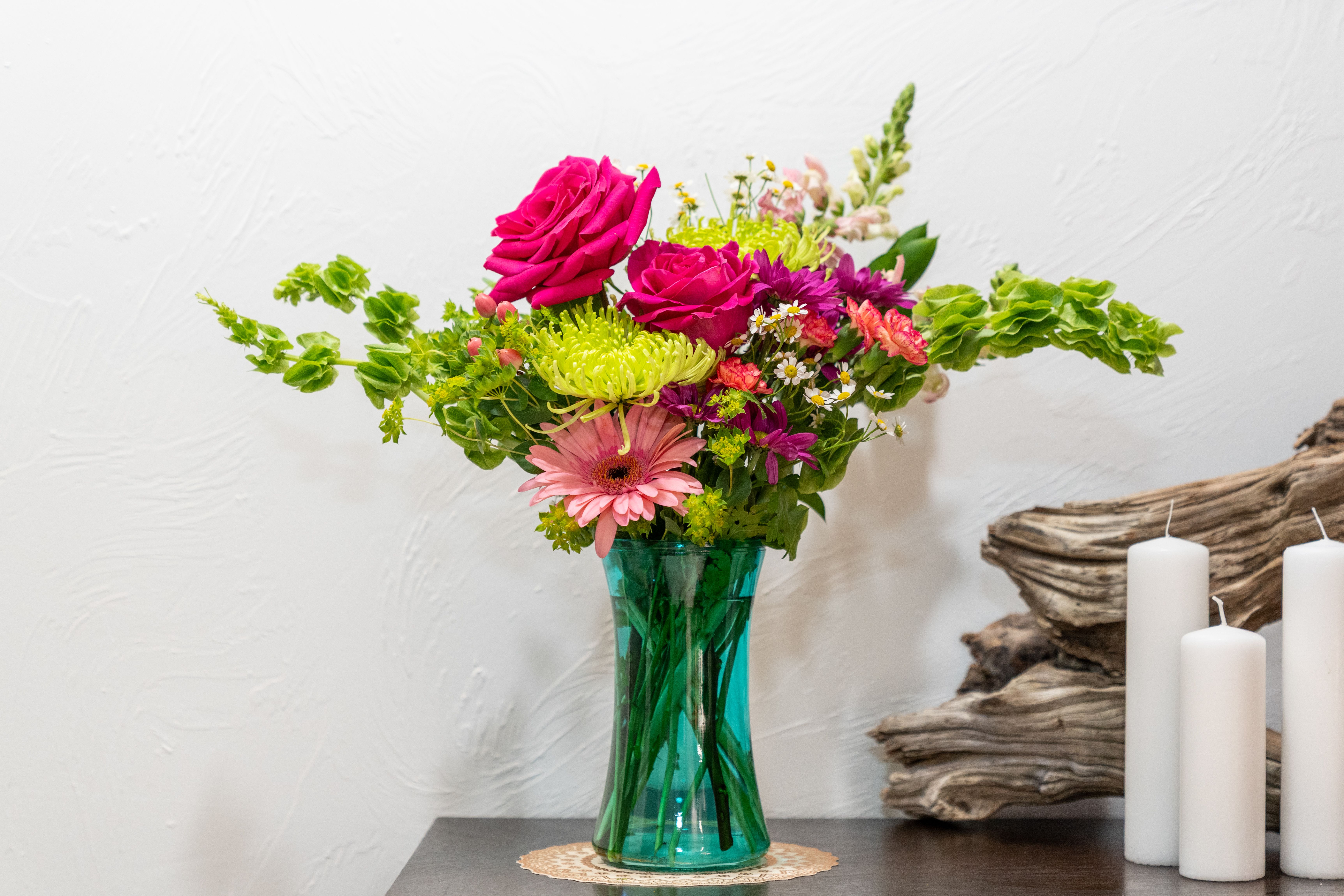 Colorful bouquet in a teal glass vase with candles beside it