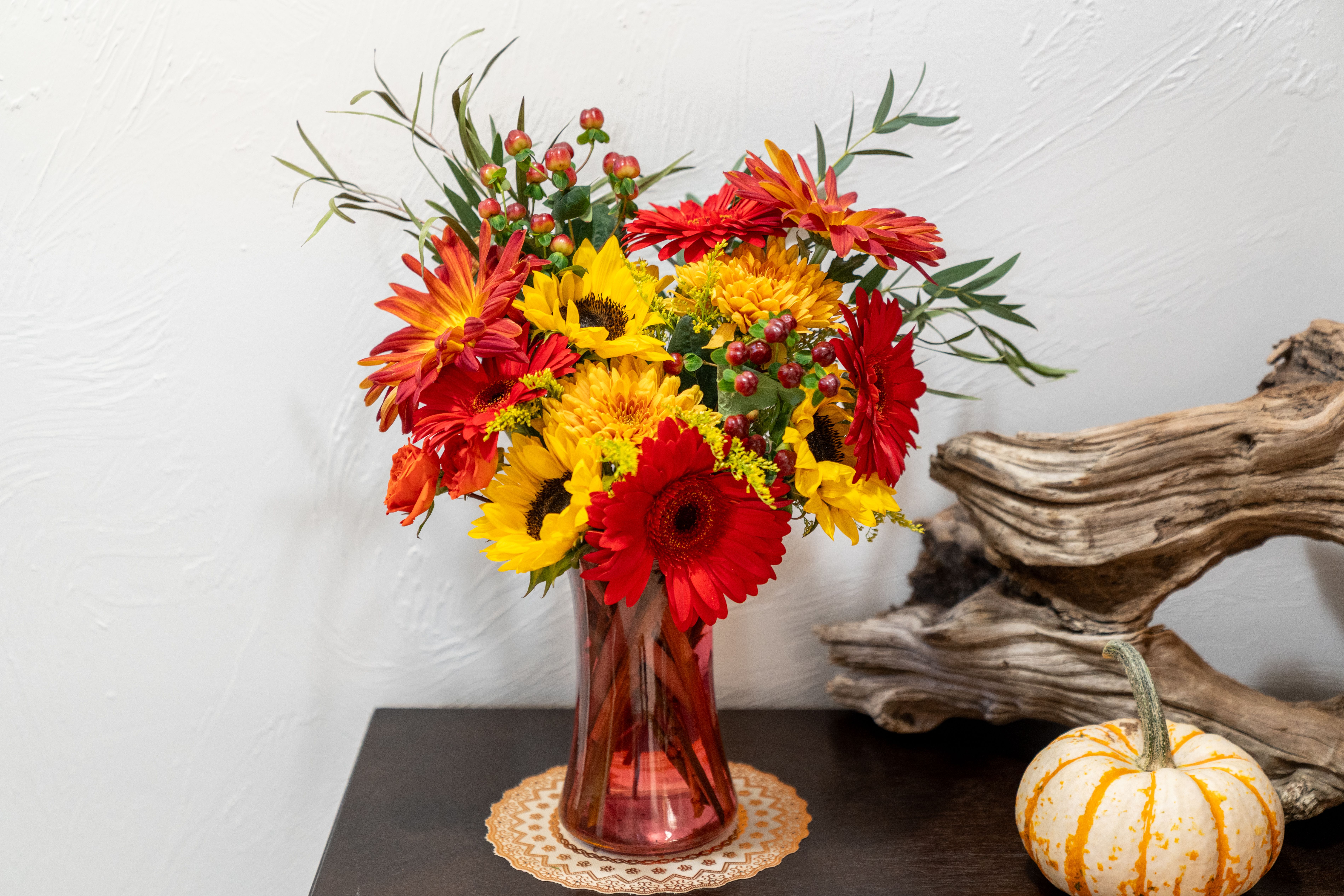 Bright mixed bouquet of sunflowers, gerbera daisies, and mums in a red glass vase