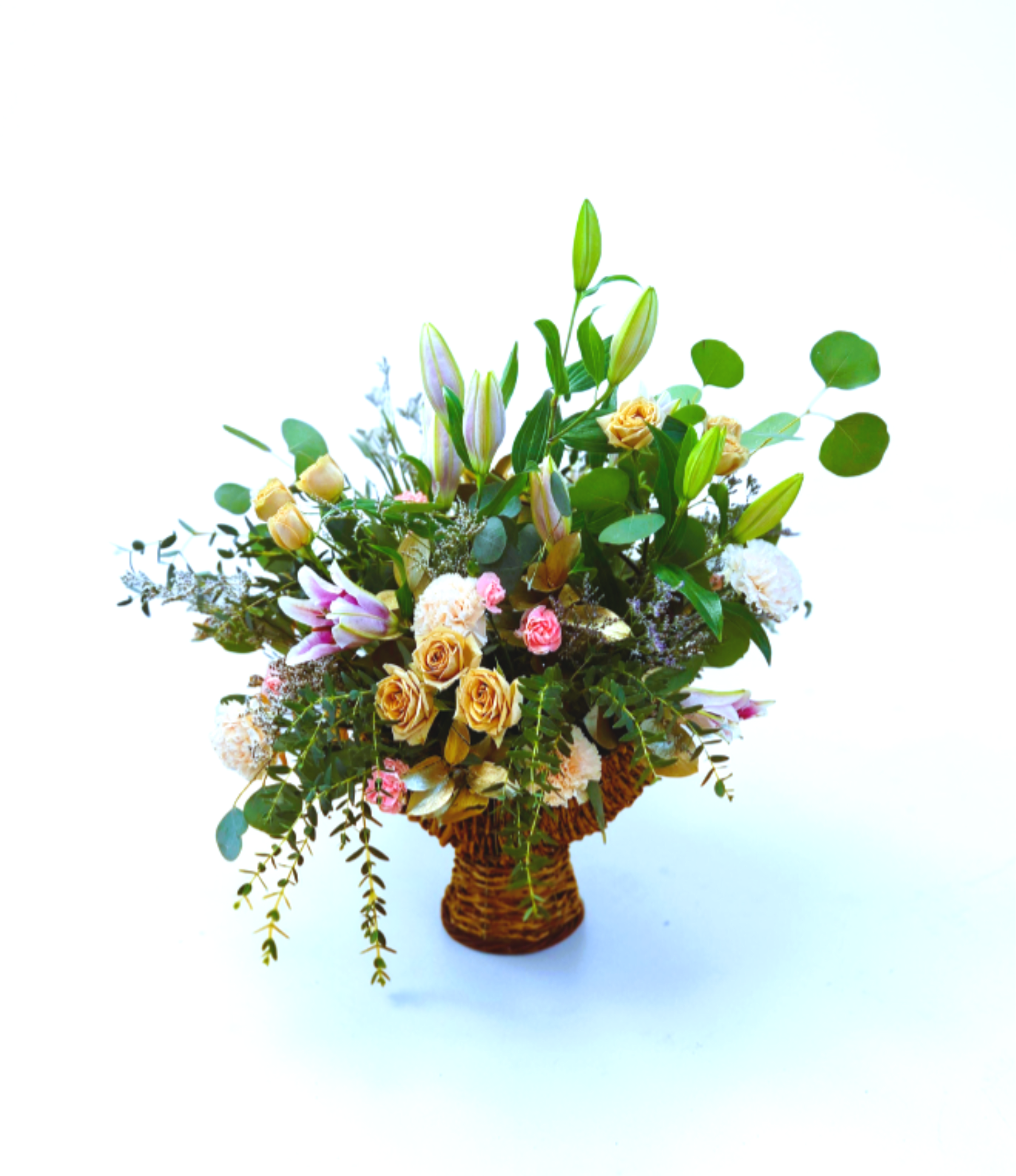 Basket arrangement of peach roses, pink lilies, and mixed blooms with tall buds.