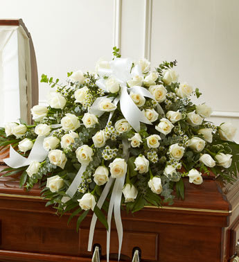 White rose casket spray with ribbon on a wooden casket