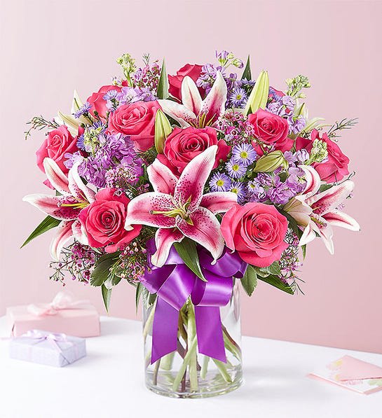 Pink roses and lilies in a glass vase with a purple ribbon