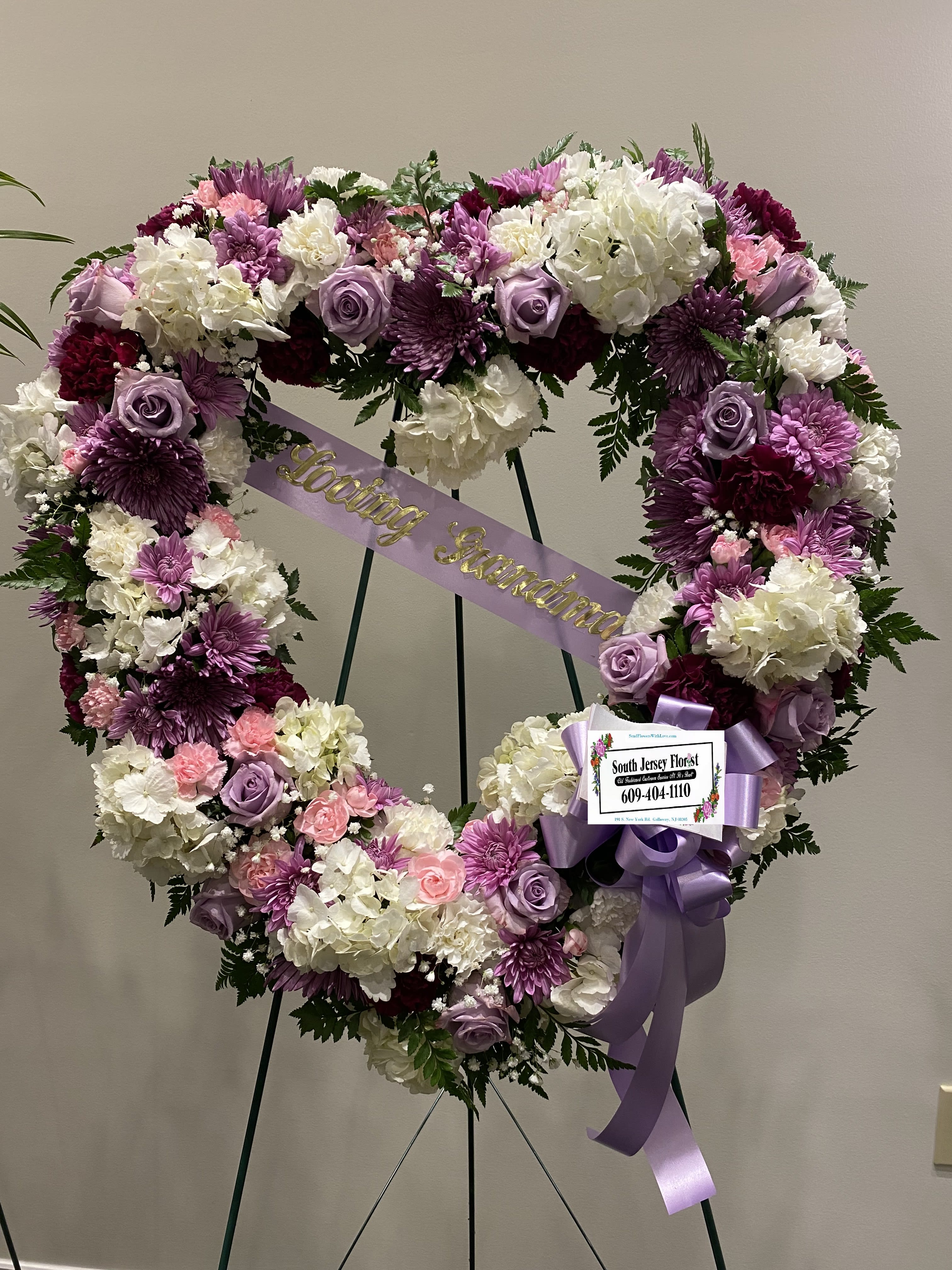 Heart-shaped floral wreath with purple, pink, and white flowers on an easel