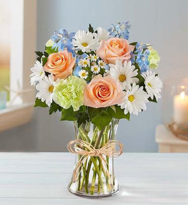 Bouquet of peach roses, white daisies, and blue flowers in a glass vase