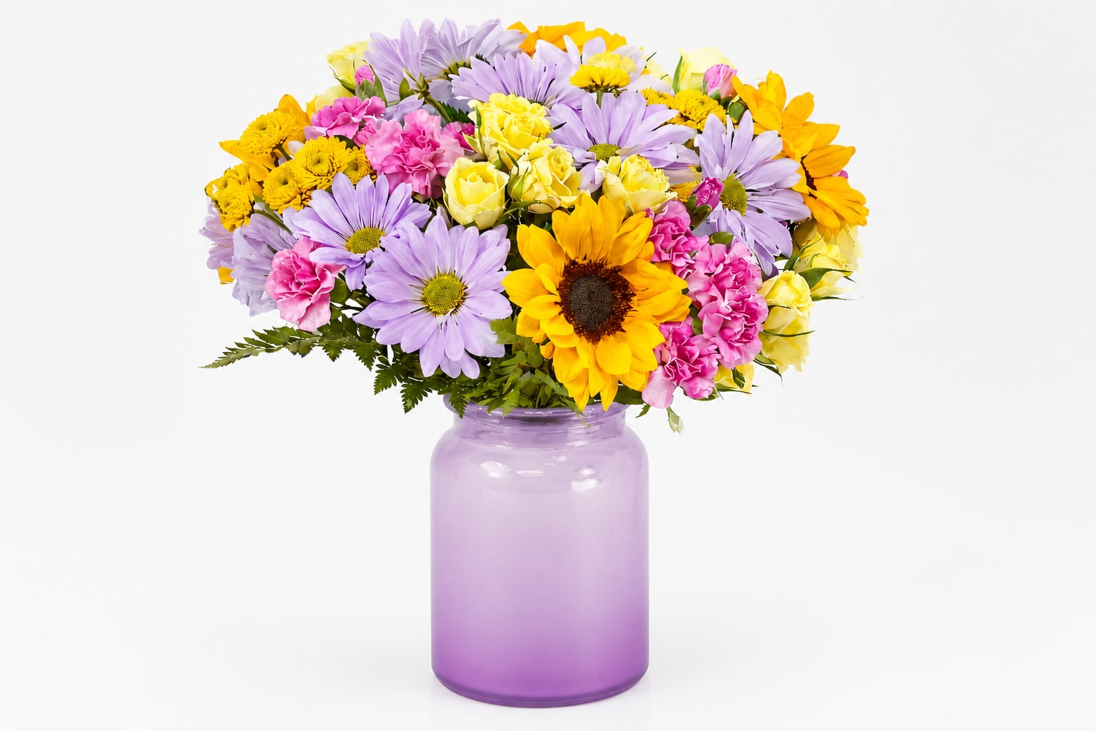 Lavender Sunrise Garden - Bright, cheerful, and beautifully balanced, Lavender Sunrise Garden brings together radiant sunflowers, soft lavender daisies, delicate pink carnations, and buttery yellow roses in a stunning lavender glass vase. This vibrant arrangement captures the warmth of sunshine and the calm of pastel blooms—making it the perfect gift to celebrate birthdays, say thank you, or simply brighten someone’s day with a fresh pop of color.
