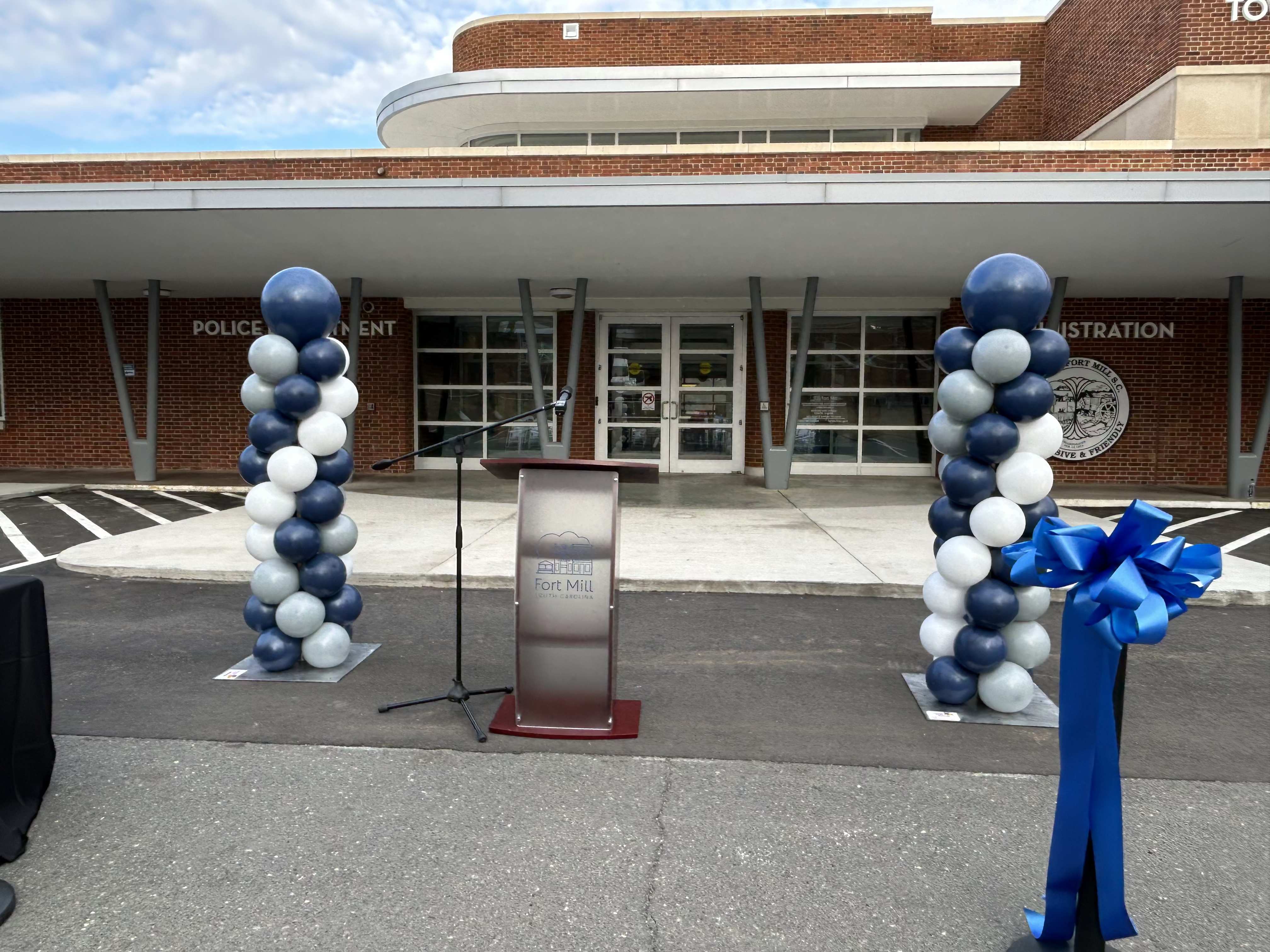 Blue and white balloon columns flank a podium outside a building.