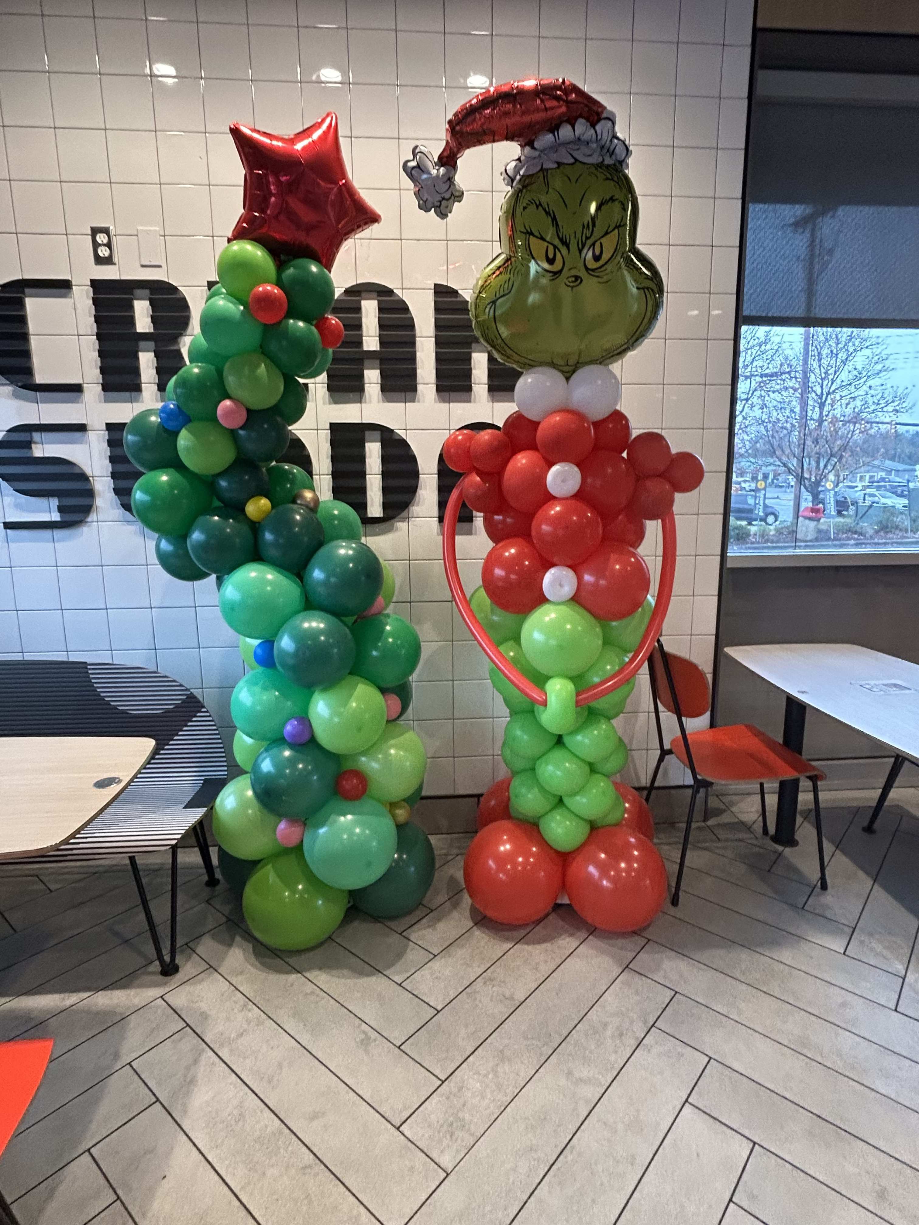 Two balloon sculptures, one Grinch-themed, standing indoors