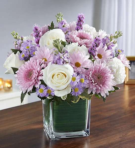 Healing Tears   Lavender &amp; White  - Sometimes in soothing the tears of another, we soothe our own sadness, as well. Our sympathy arrangement of calming lavender stock, daisy poms, white roses and carnations, expertly gathered together in a clear glass cube lined with Ti leaf ribbon, is a graceful gesture of comfort and healing.