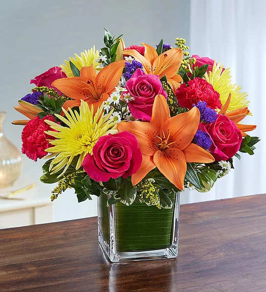 Healing Tears  Multicolor Bright - It’s hard to know how to console in a time of darkness, but sometimes a gesture of color can make a small, yet deeply appreciated difference. Our sympathy arrangement of sprightly pink roses, carnations, orange lilies and yellow mums, expertly gathered together in a clear glass cube lined with a Ti leaf ribbon, is an uplifting gesture of comfort and healing.