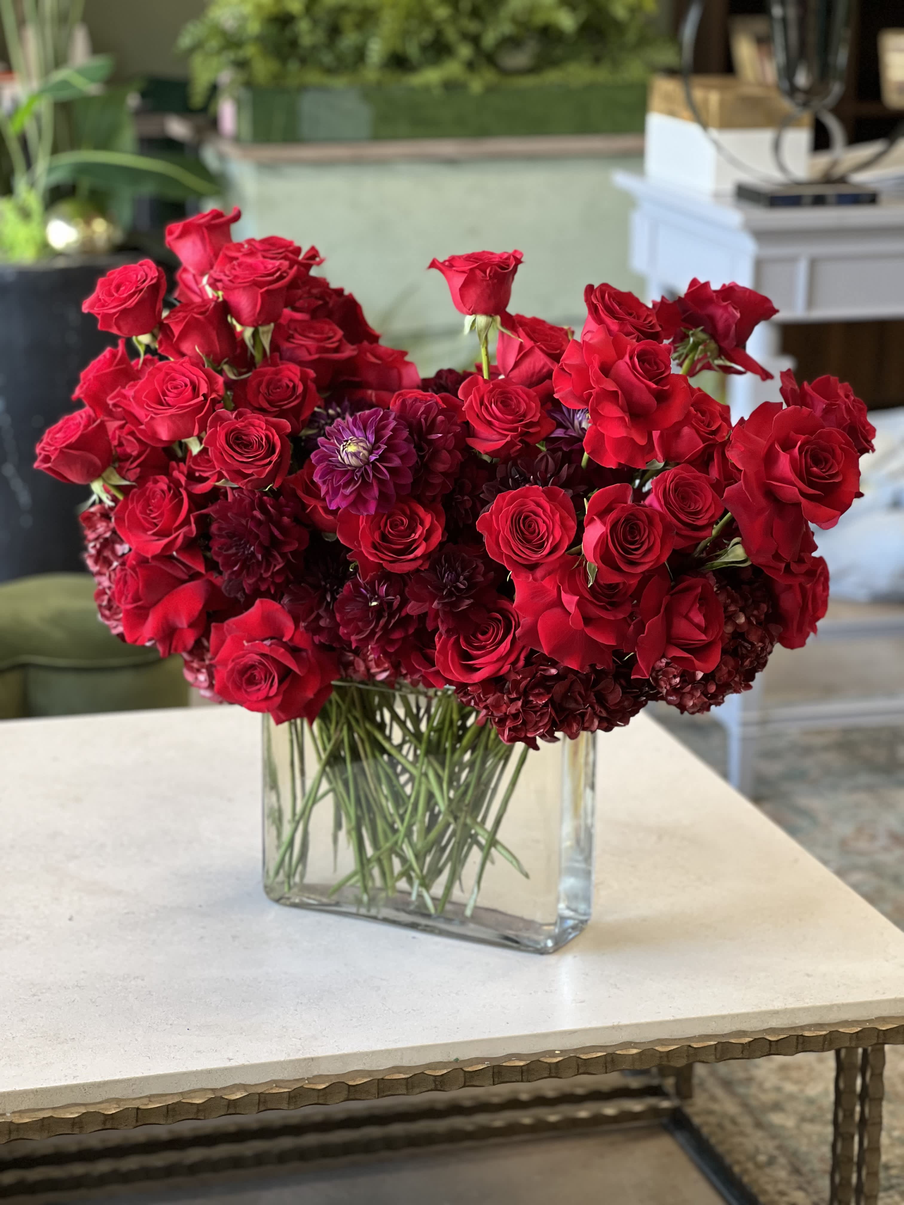 Red roses and dark purple blooms arranged in a clear rectangular vase