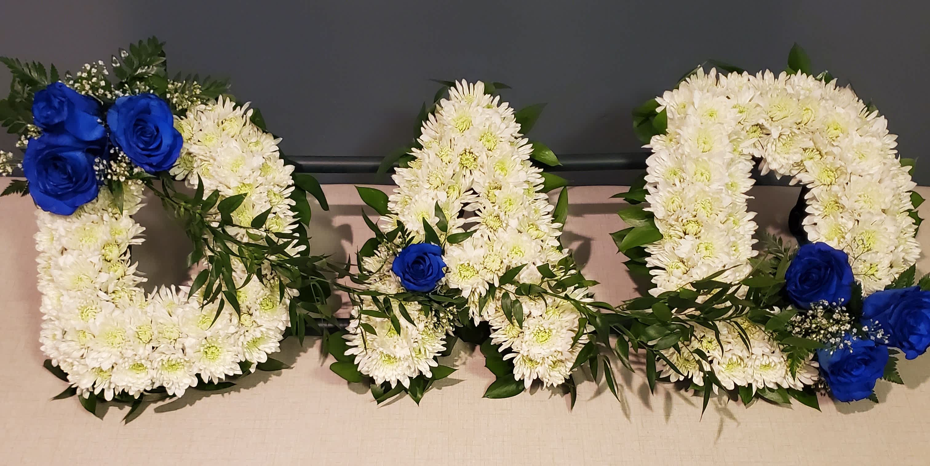 Three floral letters made of white flowers with blue roses and greenery accents.