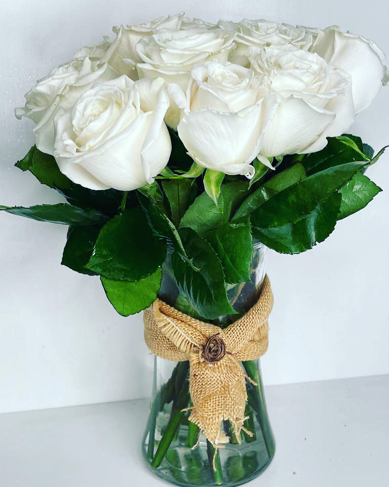 White roses arranged in a glass vase with a burlap ribbon