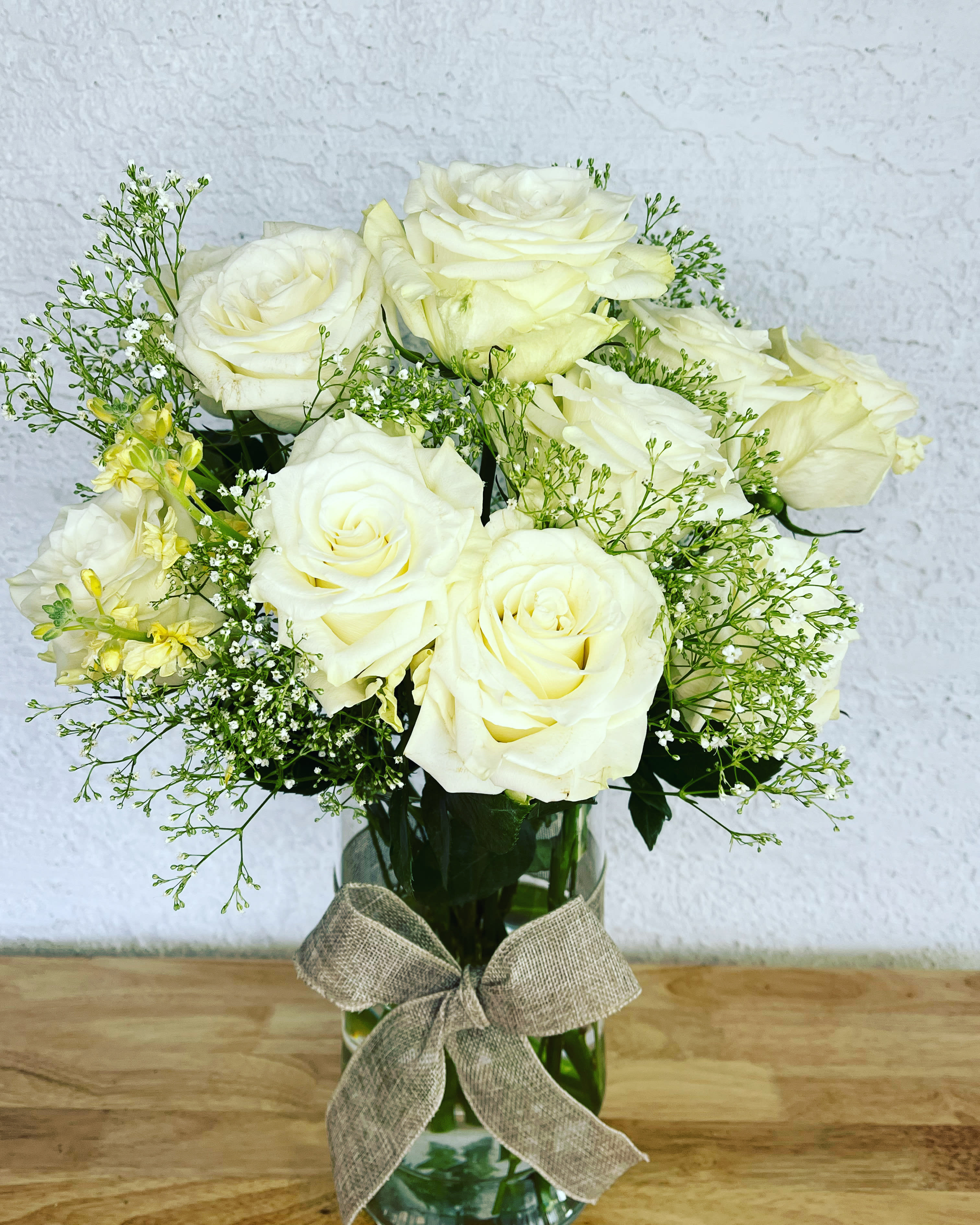 White roses arranged in a glass vase with a burlap bow