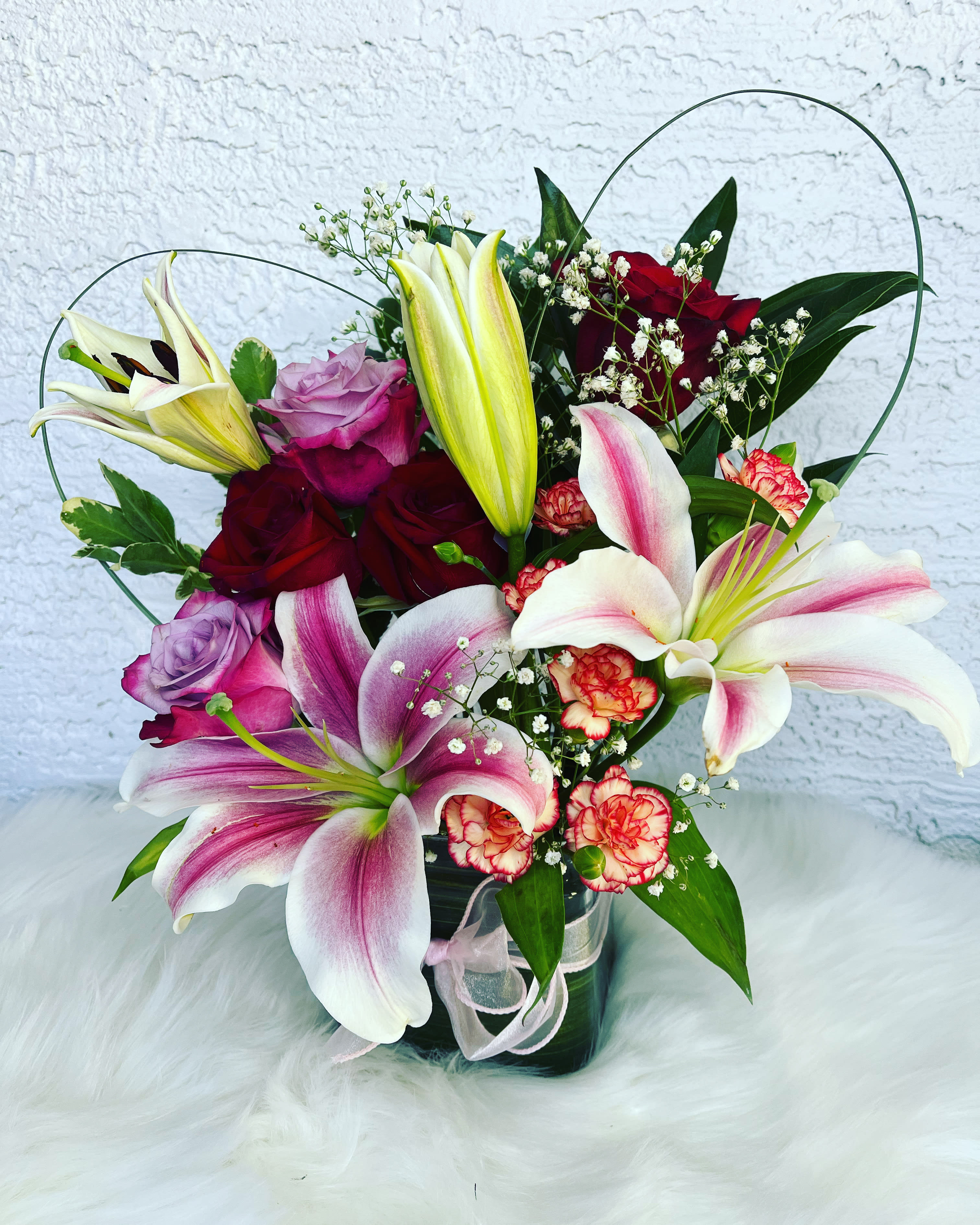 Bouquet of lilies and roses in a glass vase with pink ribbon
