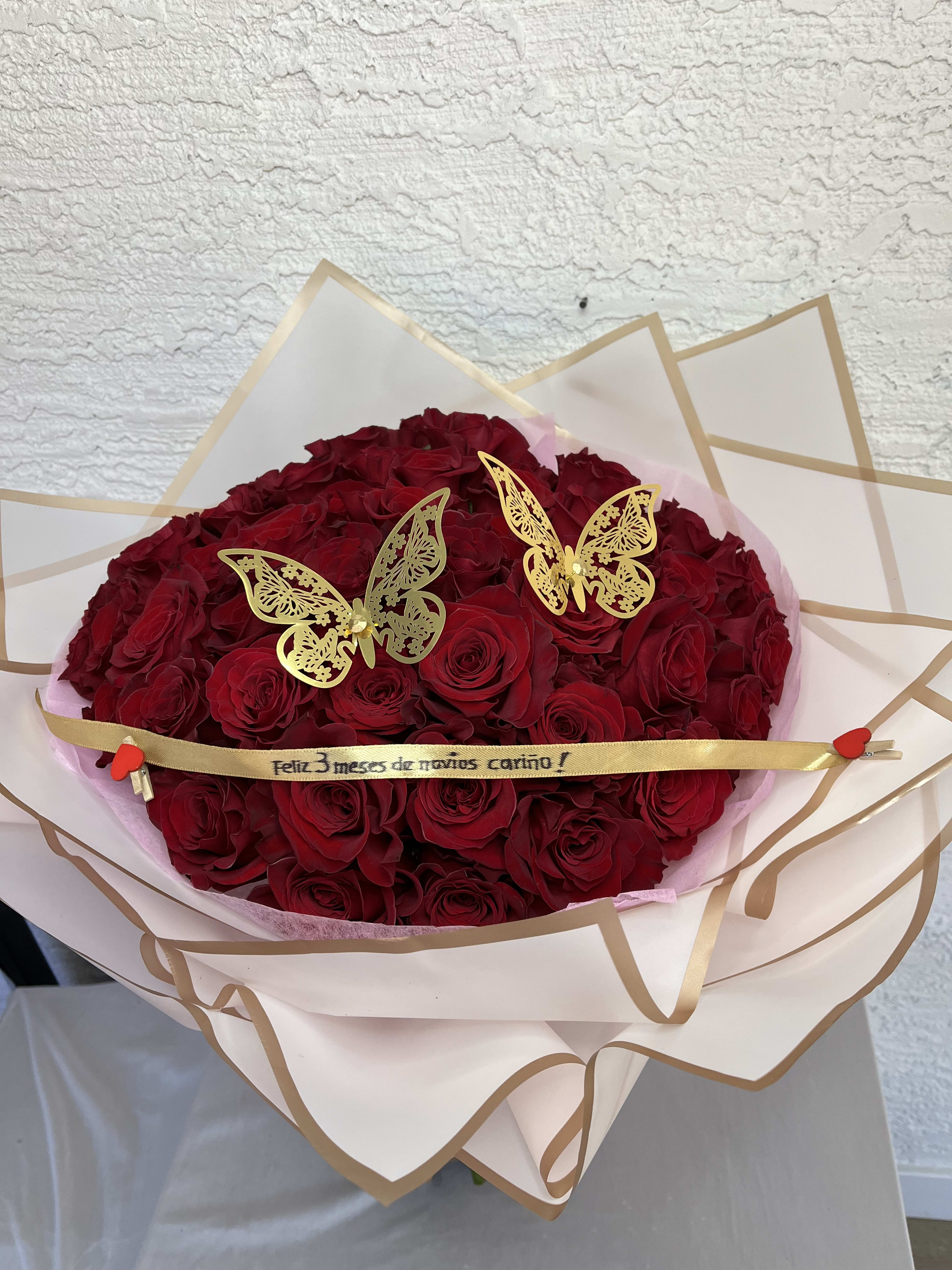 Bouquet of red roses wrapped in cream paper with gold trim and butterfly picks