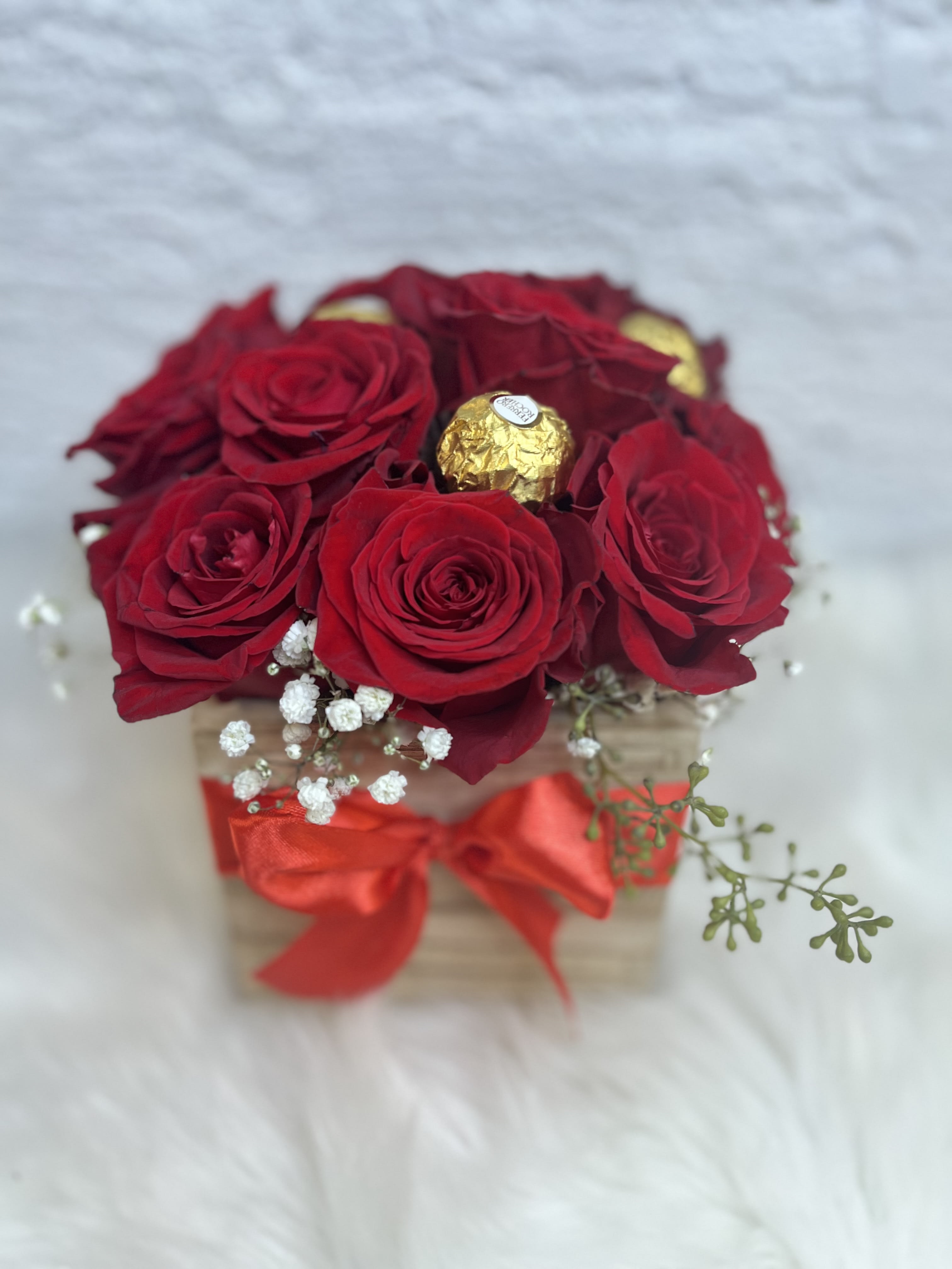 Red roses in a small box with a red ribbon and gold chocolates