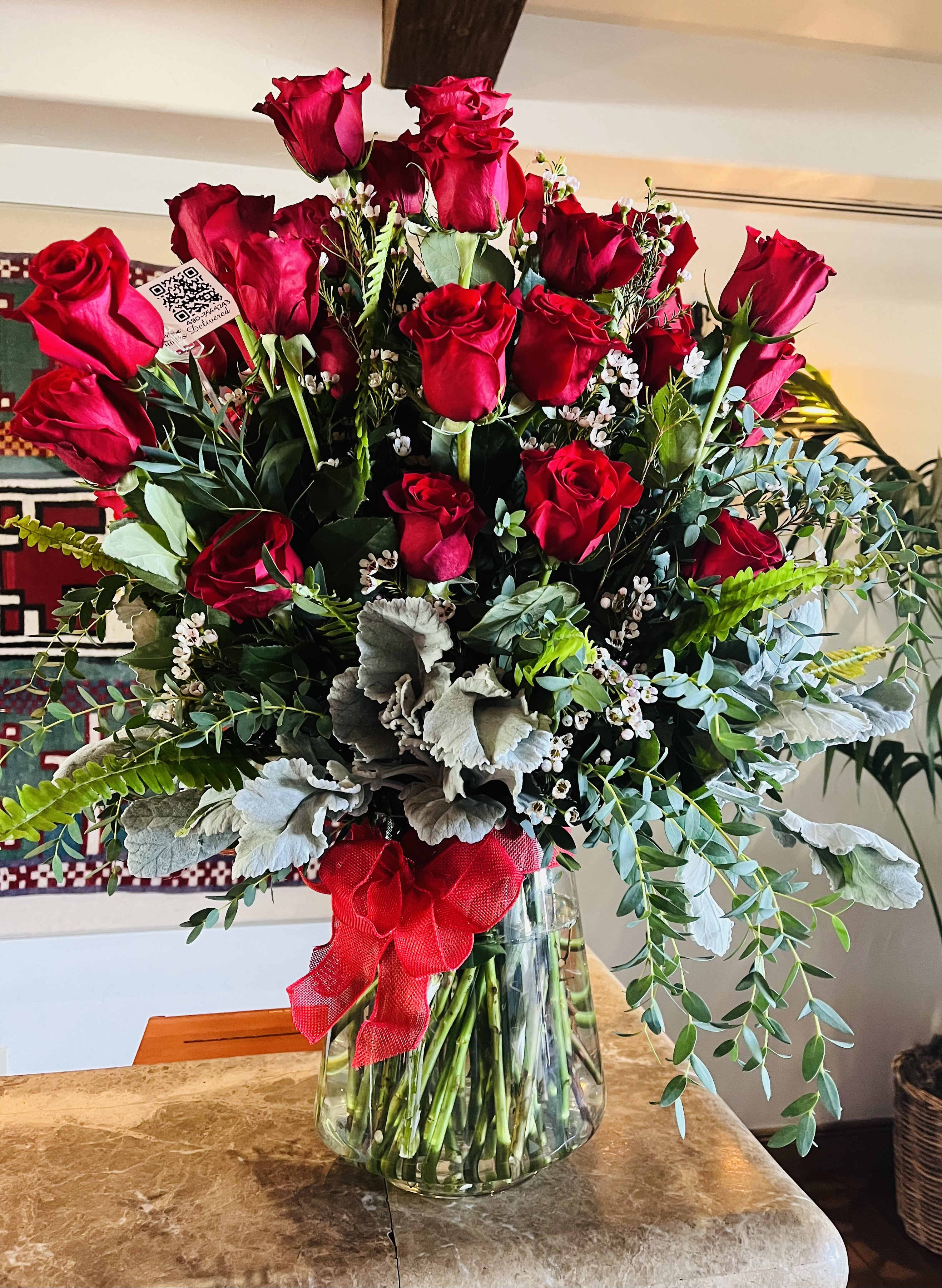 Red roses arranged in a clear glass vase with greenery and a red ribbon