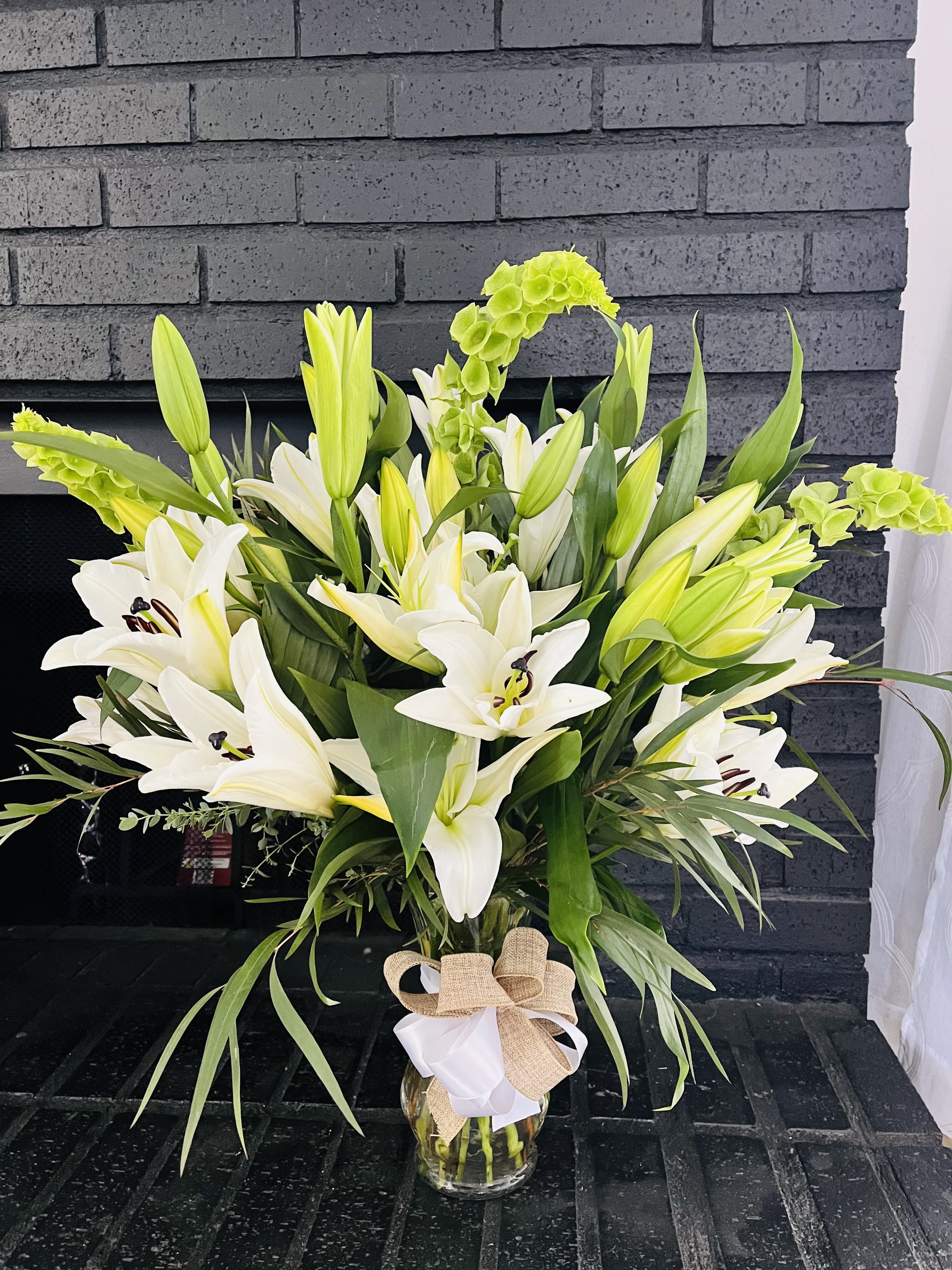 White lilies and green blooms in a glass vase with a burlap bow