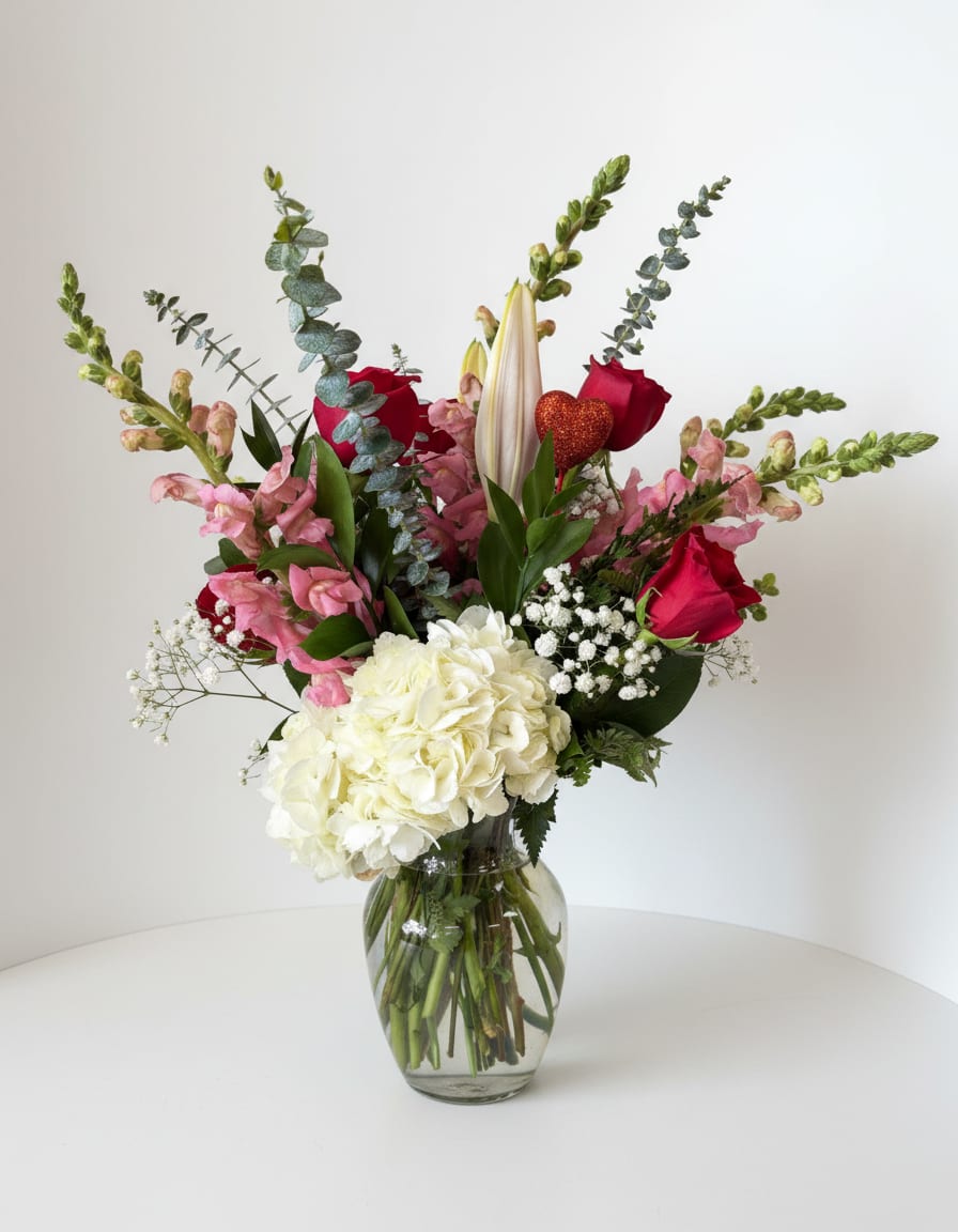 Mixed bouquet with red roses, white hydrangea, pink blooms, and a glass vase