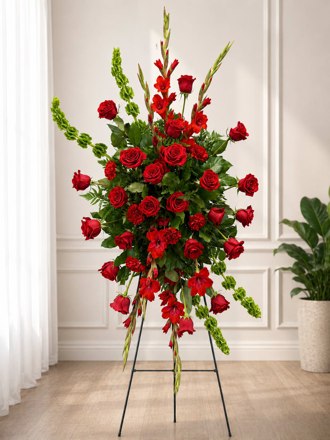 Tall standing arrangement of red roses and red flowers with green accents