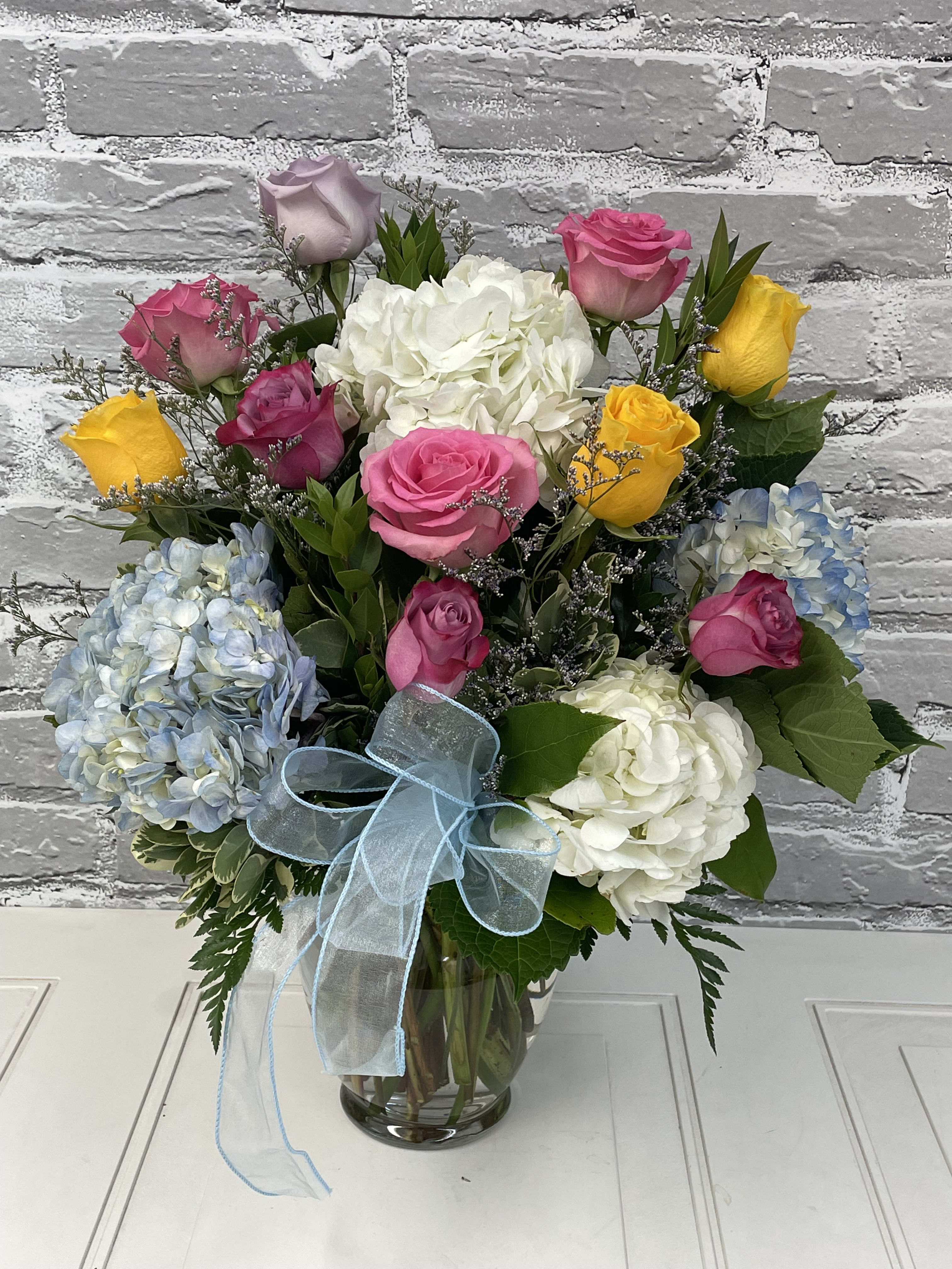 Bouquet of roses and hydrangeas in a glass vase with a blue ribbon