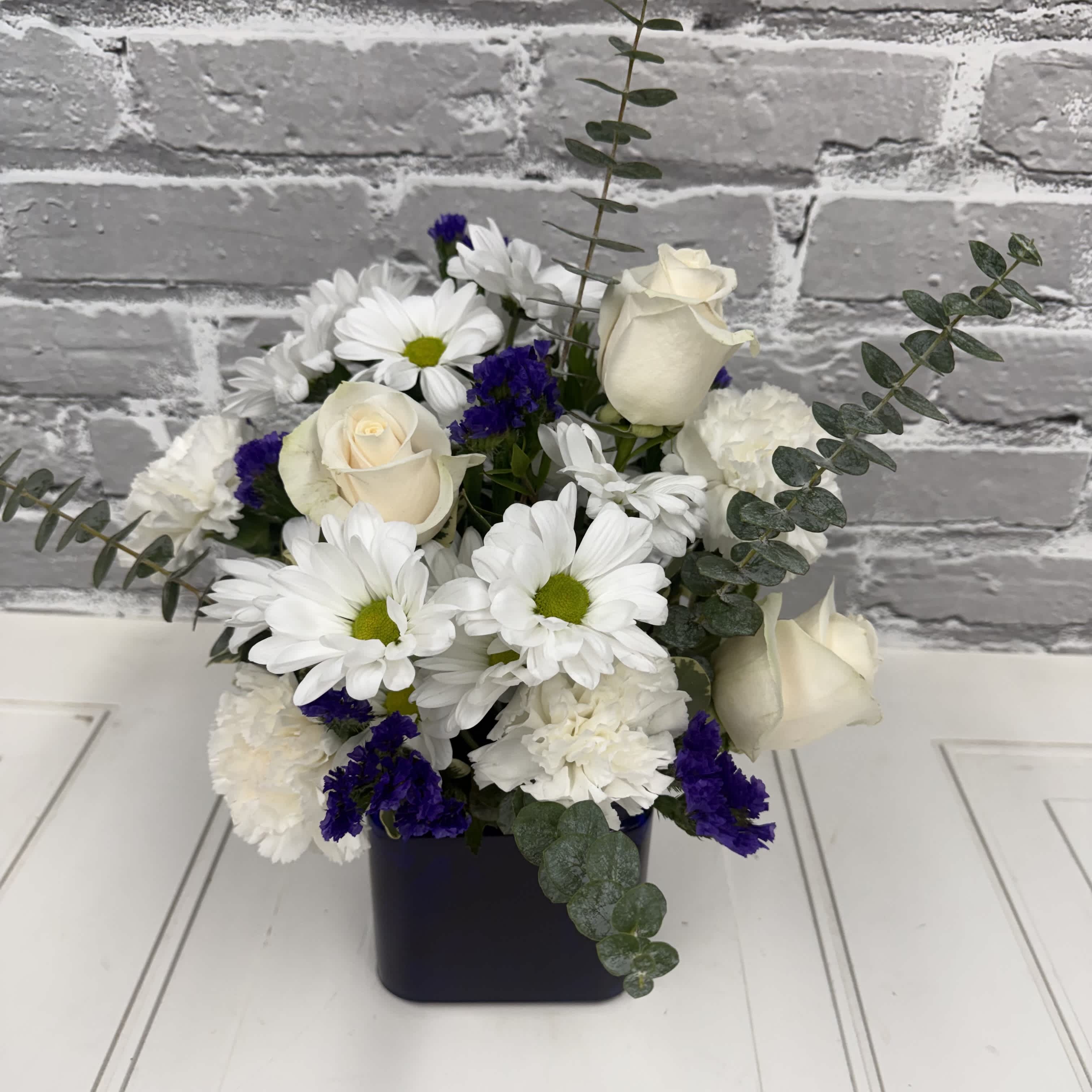 White roses and daisies arranged in a black square vase