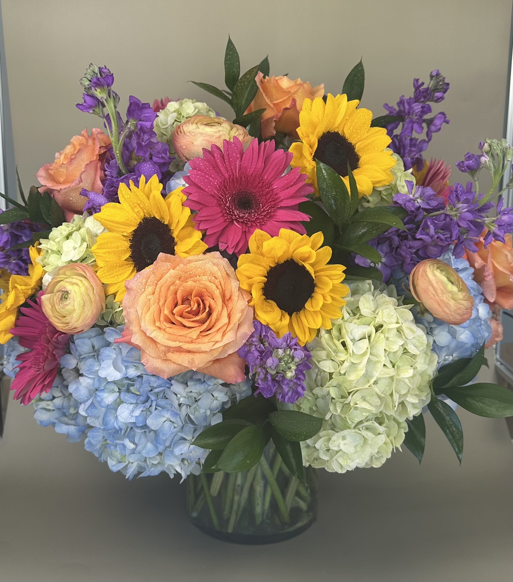 Colorful bouquet with sunflowers, roses, gerbera daisies, and hydrangeas in a glass vase