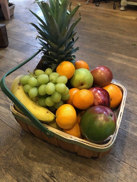 Basket of assorted fruit with a pineapple, grapes, bananas, oranges, apples, and a pear