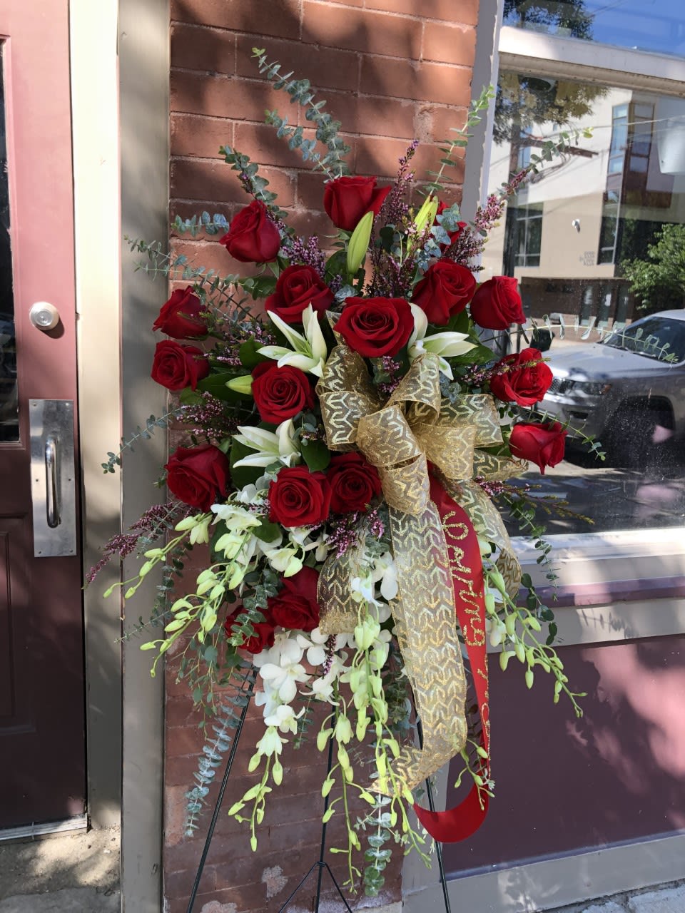 Tall standing arrangement of red roses and white lilies with a gold ribbon