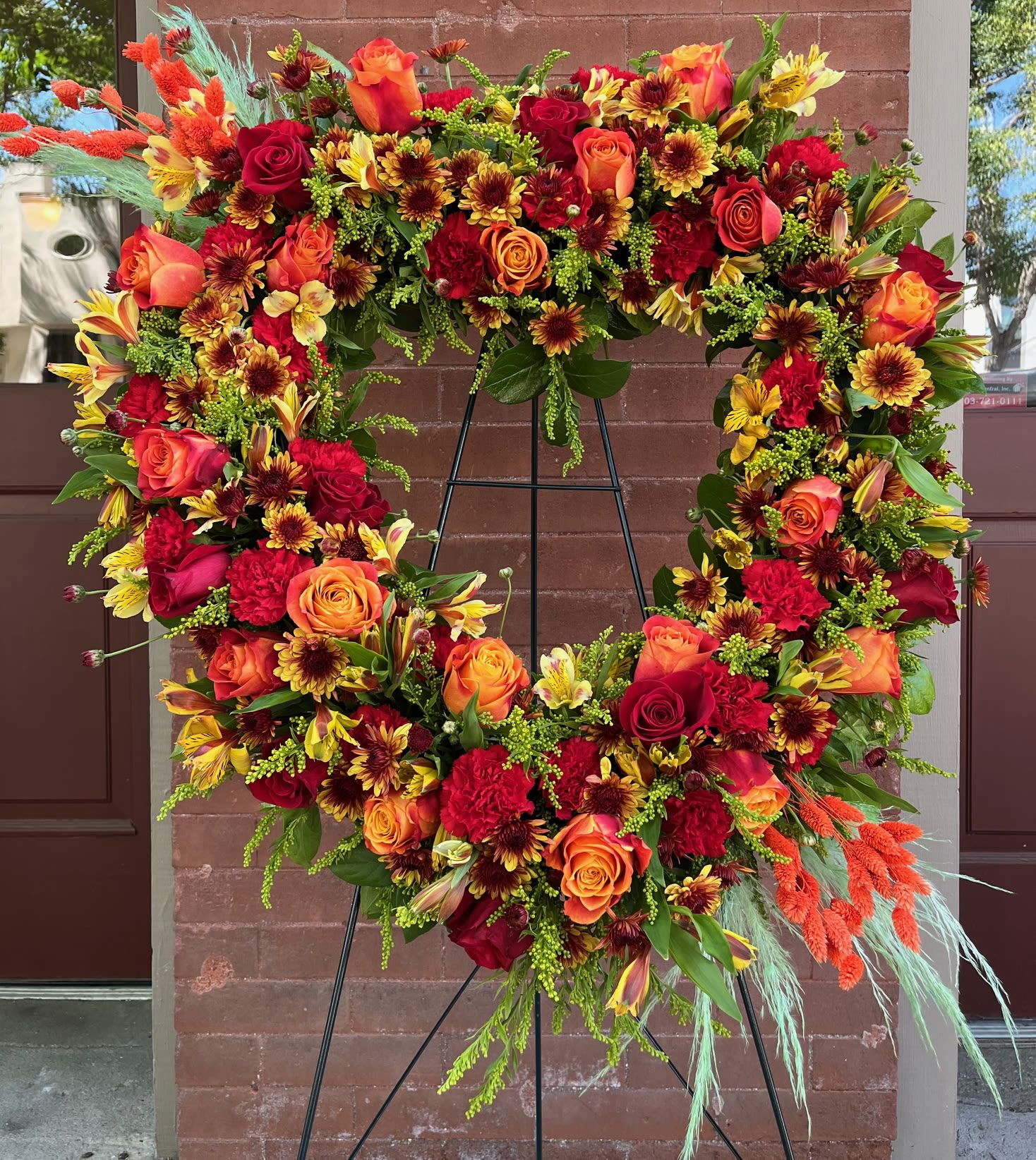 Large floral wreath with red, orange, and yellow blooms on a black stand