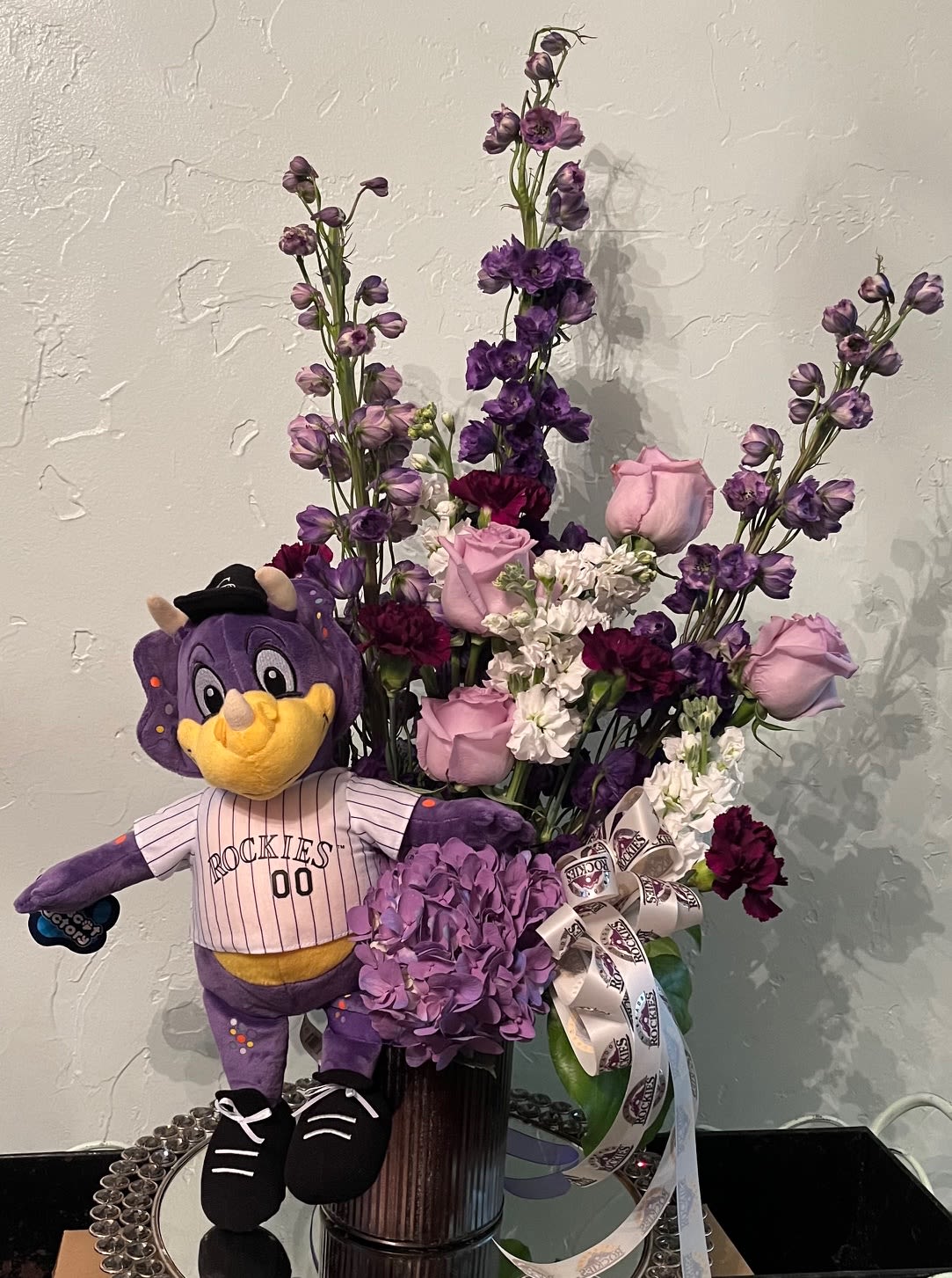 Purple floral arrangement with a Rockies mascot plush in a vase