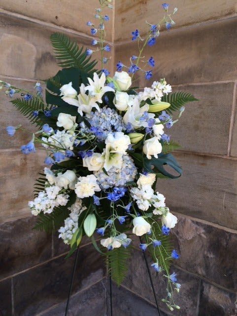 Tall standing spray of white lilies and roses with blue flowers on an easel