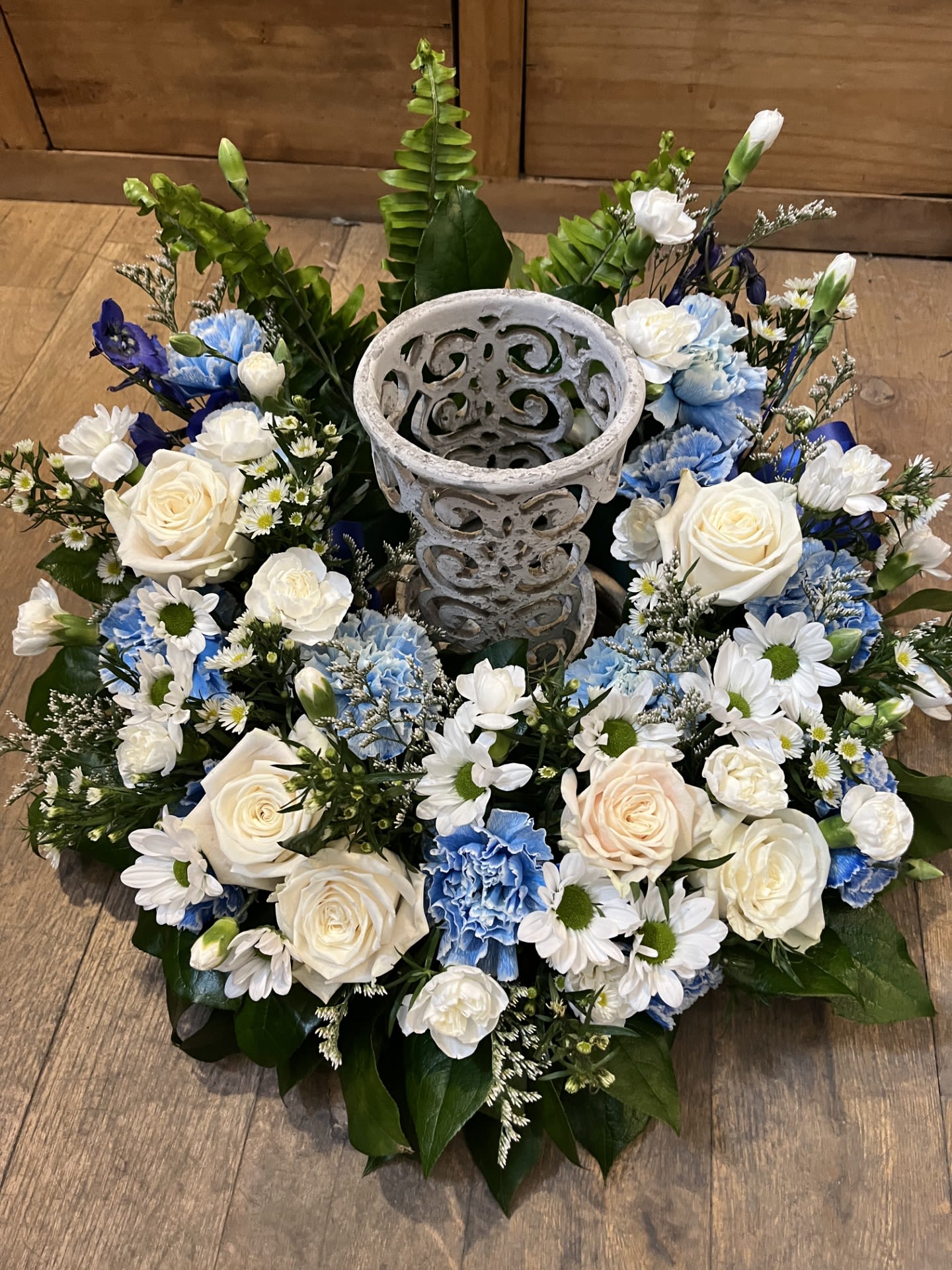 Circular floral wreath with white and blue flowers around a decorative stone urn