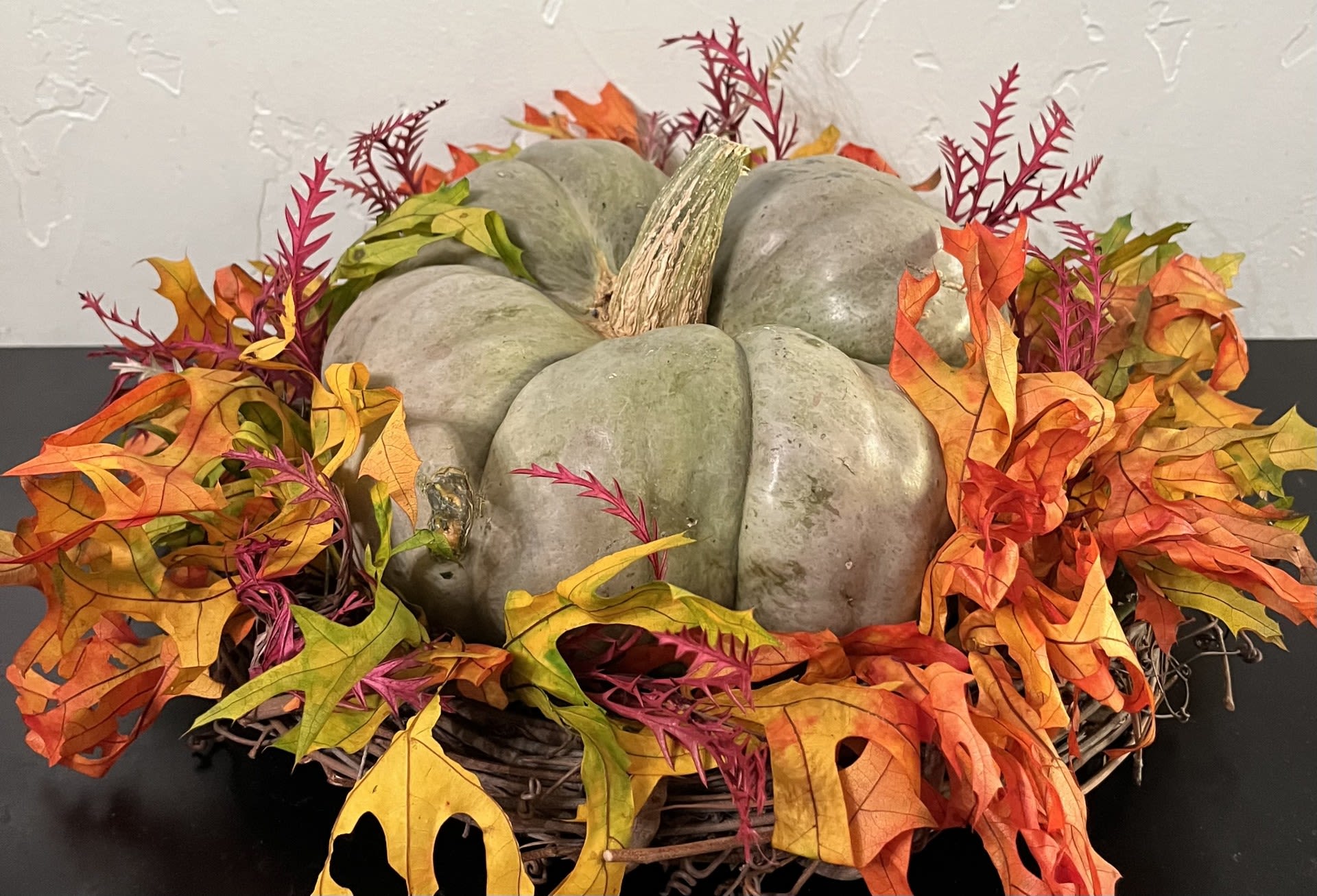Decorative pumpkin centerpiece surrounded by autumn leaves in a wicker basket