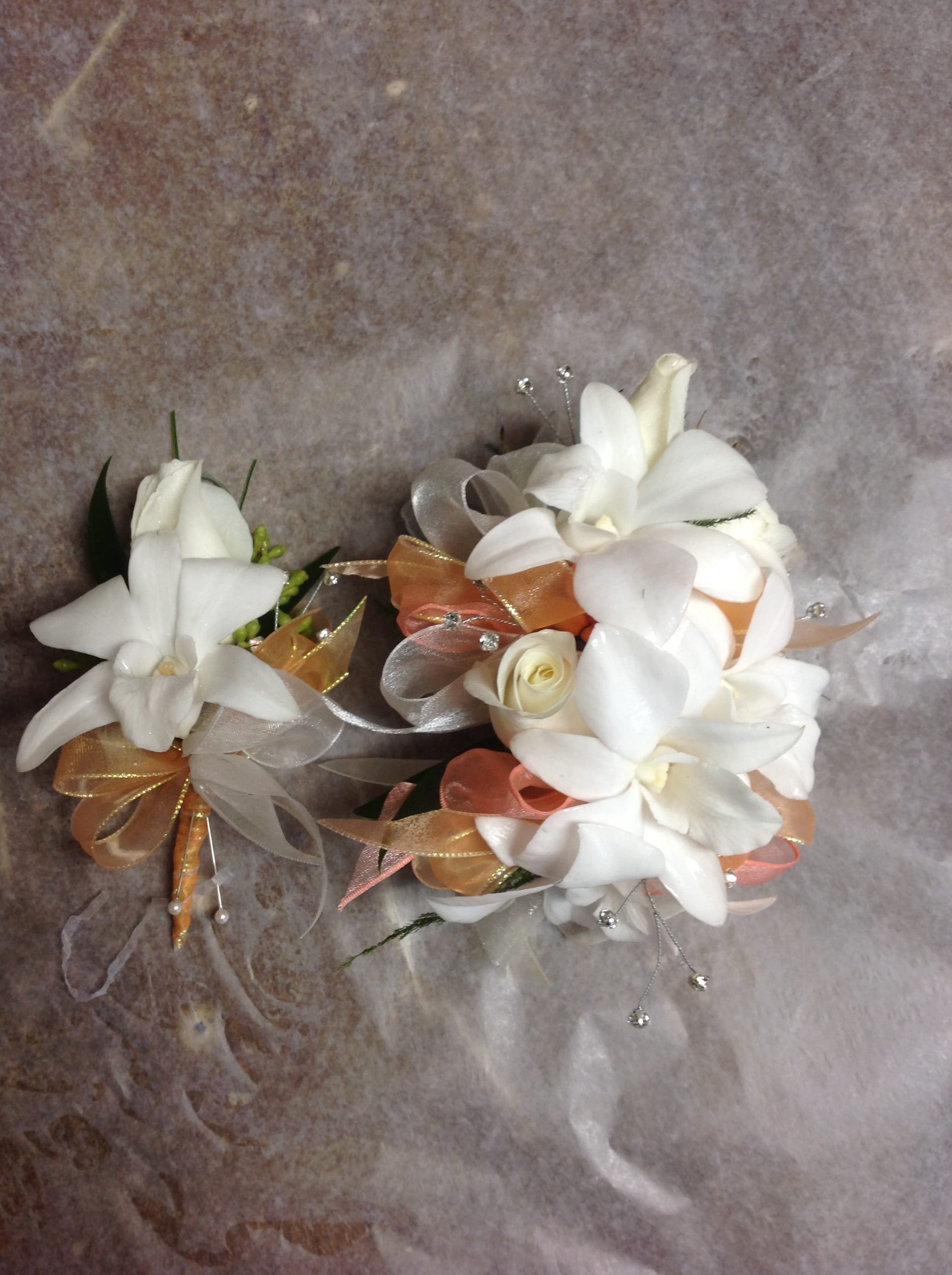 Two white floral corsages with ribbon accents on a textured background