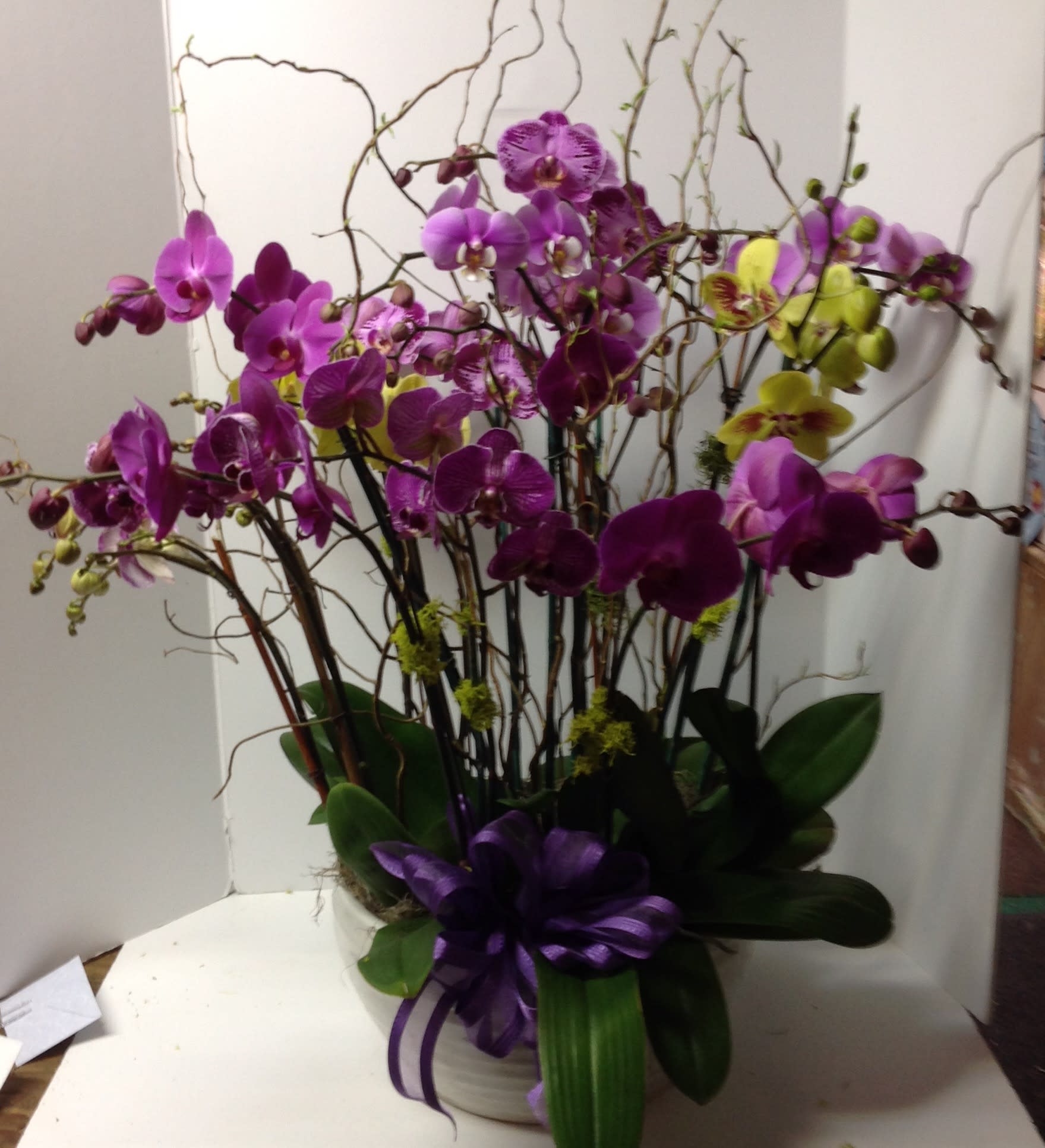 Arrangement of purple and yellow orchids in a white container with a purple ribbon