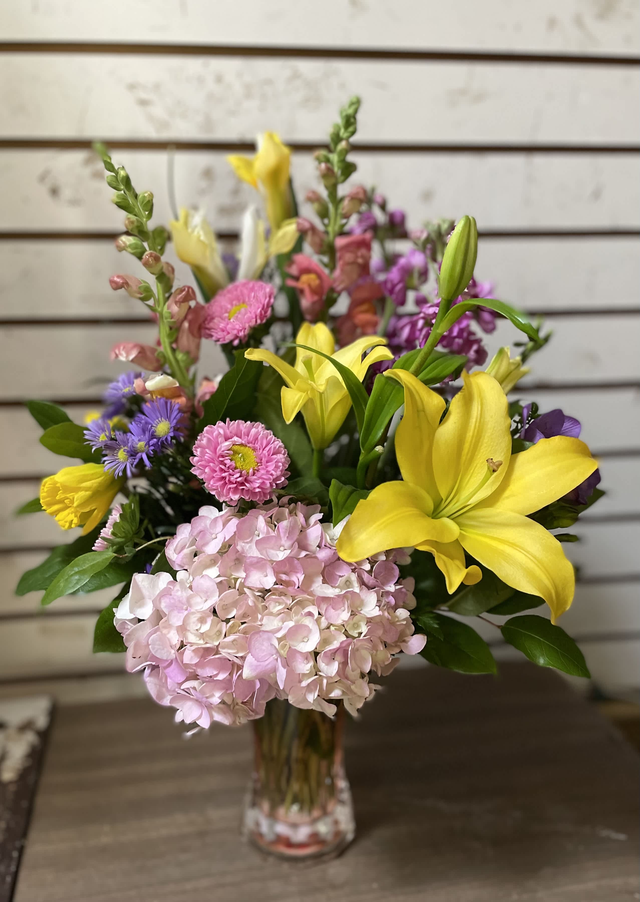 Mixed bouquet with yellow lilies, pink hydrangea, and purple flowers in a glass vase