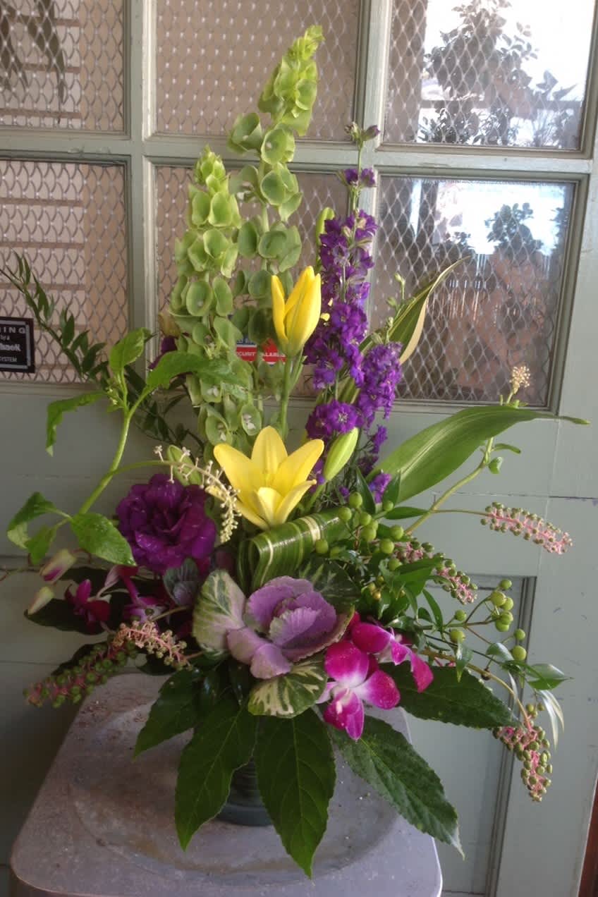 Tall mixed floral arrangement with yellow lilies, purple blooms, and green accents in a vase