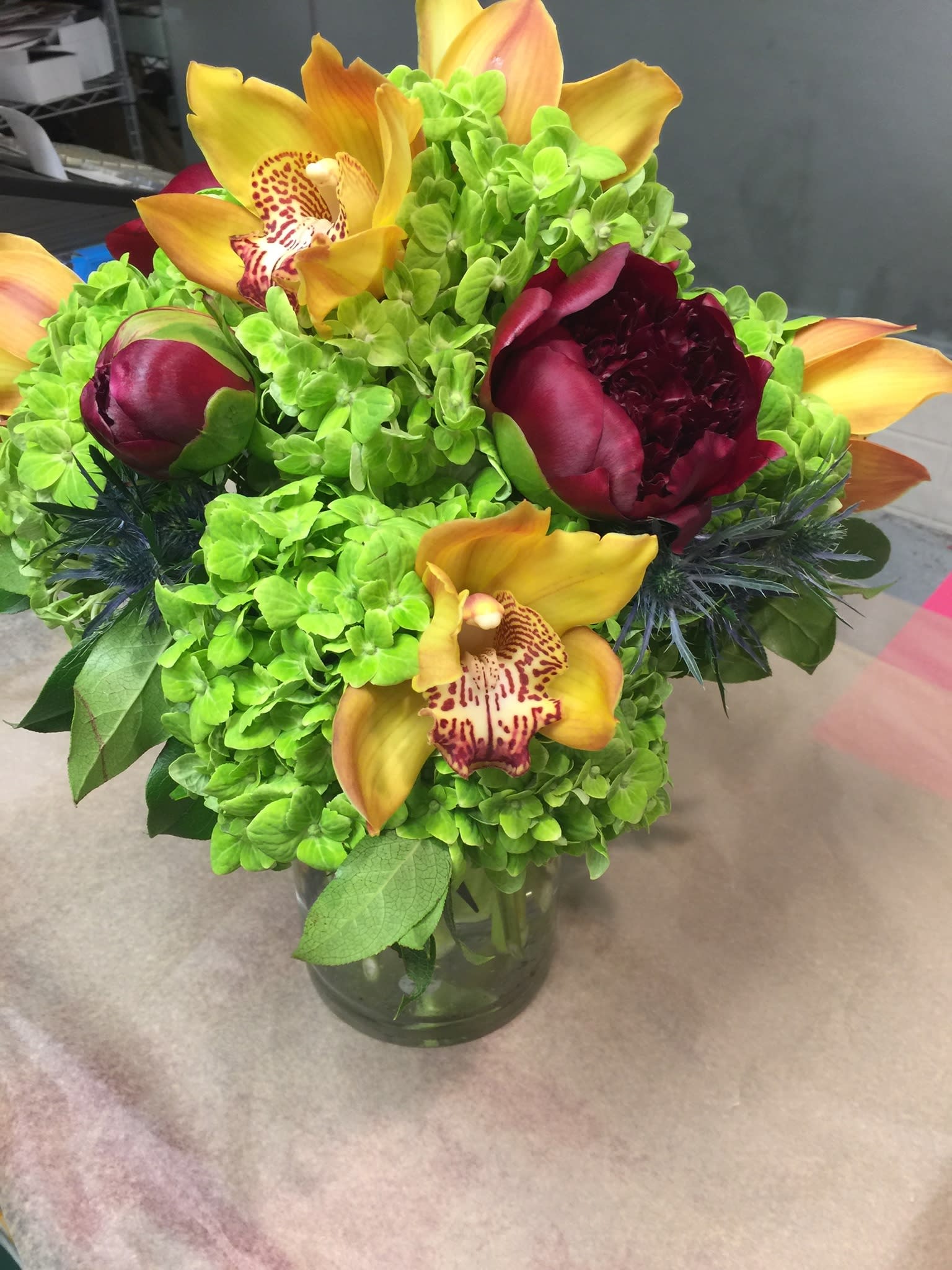 Bouquet of green hydrangeas with yellow orchids and burgundy peonies in a glass vase