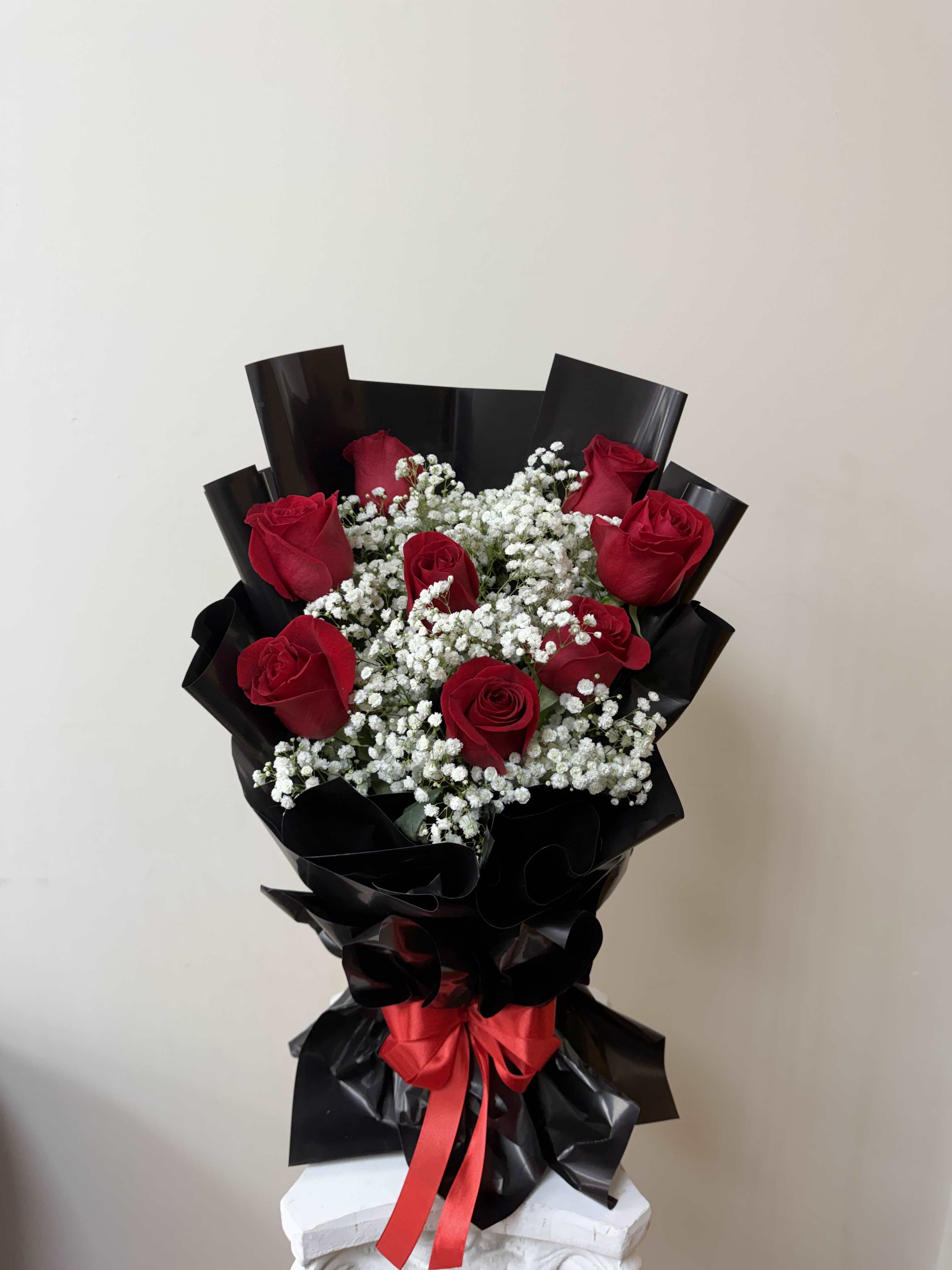 Bouquet of red roses and white baby's breath wrapped in black paper with a red ribbon