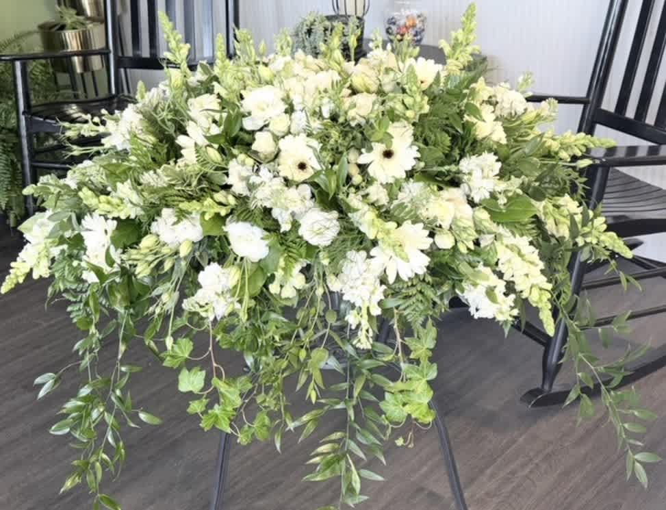 Large white floral arrangement with trailing greenery on a black stand