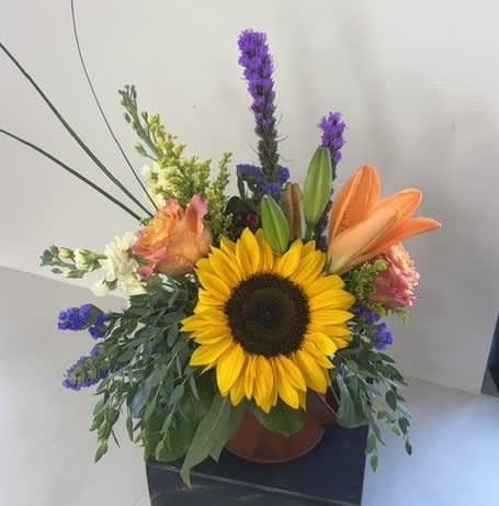 Sunflower arrangement with orange lilies and purple accents in a vase