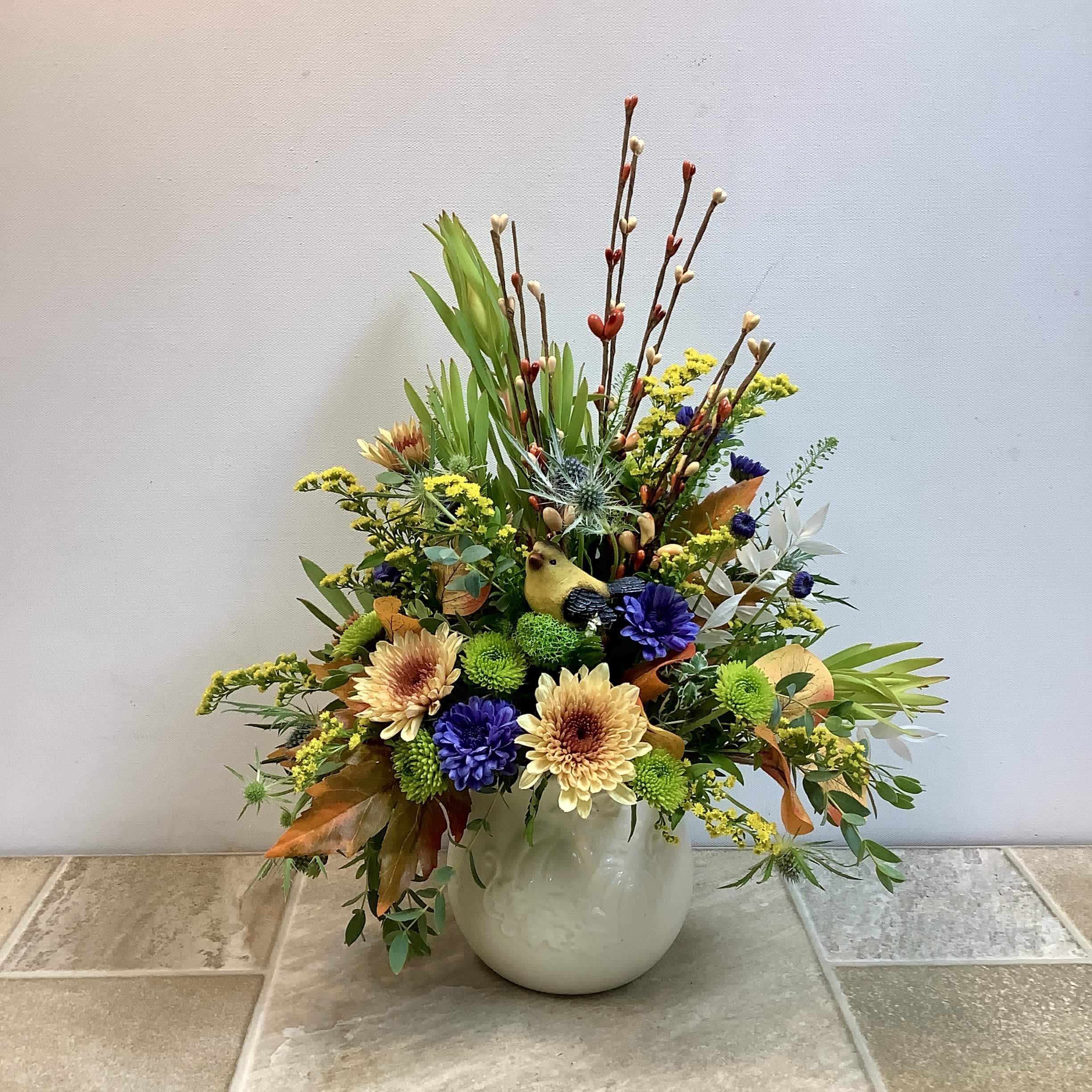 Mixed floral arrangement in a white vase with yellow, purple, and cream blooms