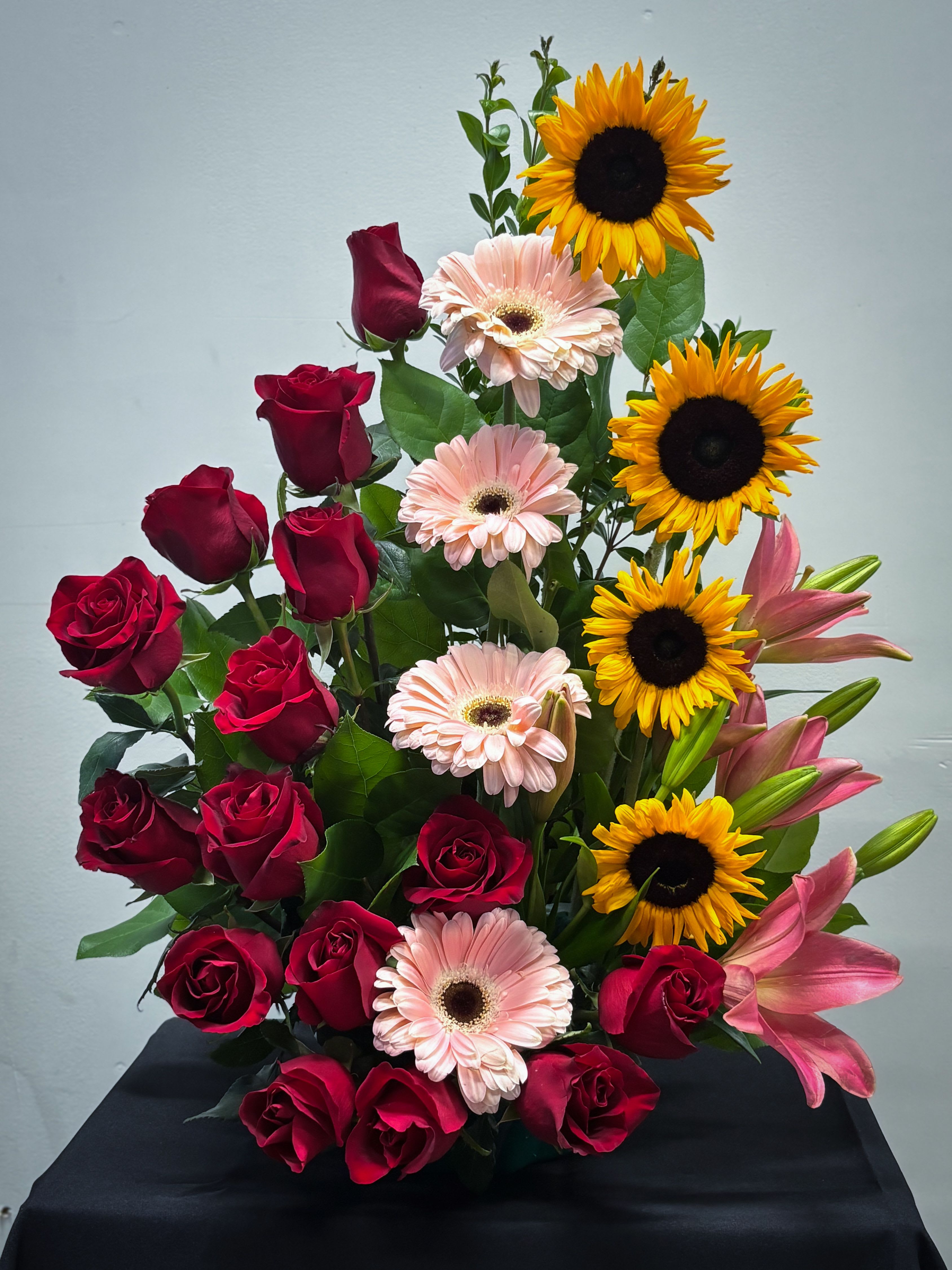 Tall arrangement of red roses, yellow sunflowers, pink gerbera daisies, and pink lilies