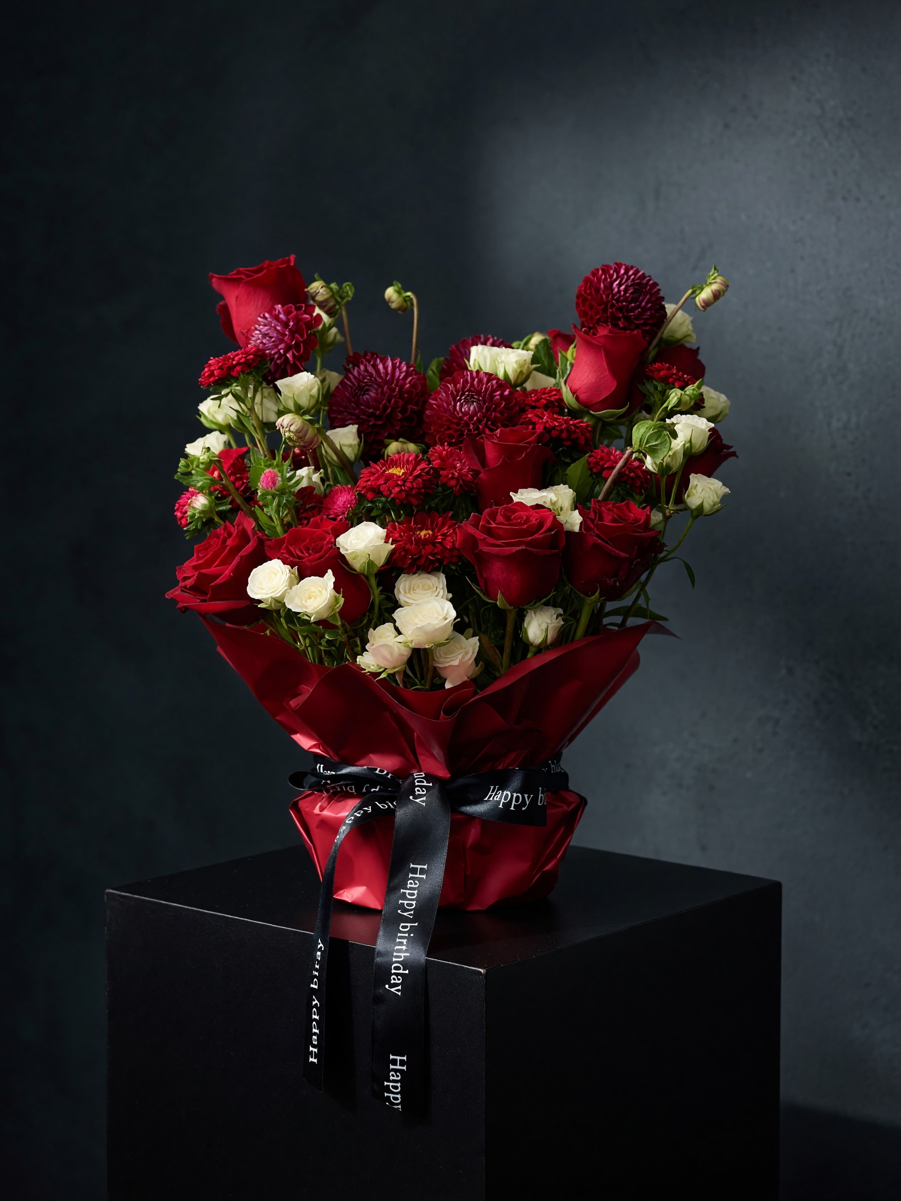 Red roses and white spray flowers in red wrap with a birthday ribbon