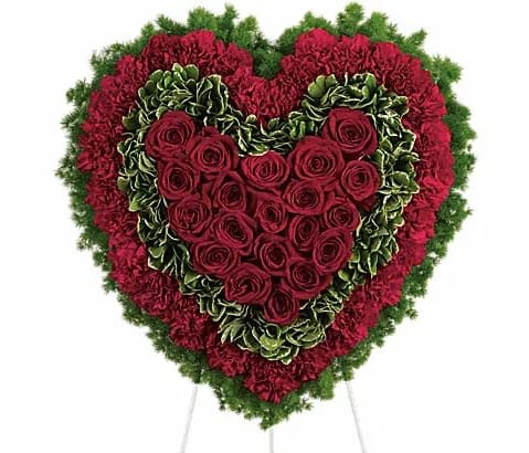 Heart-shaped floral spray with red roses and carnations on a stand